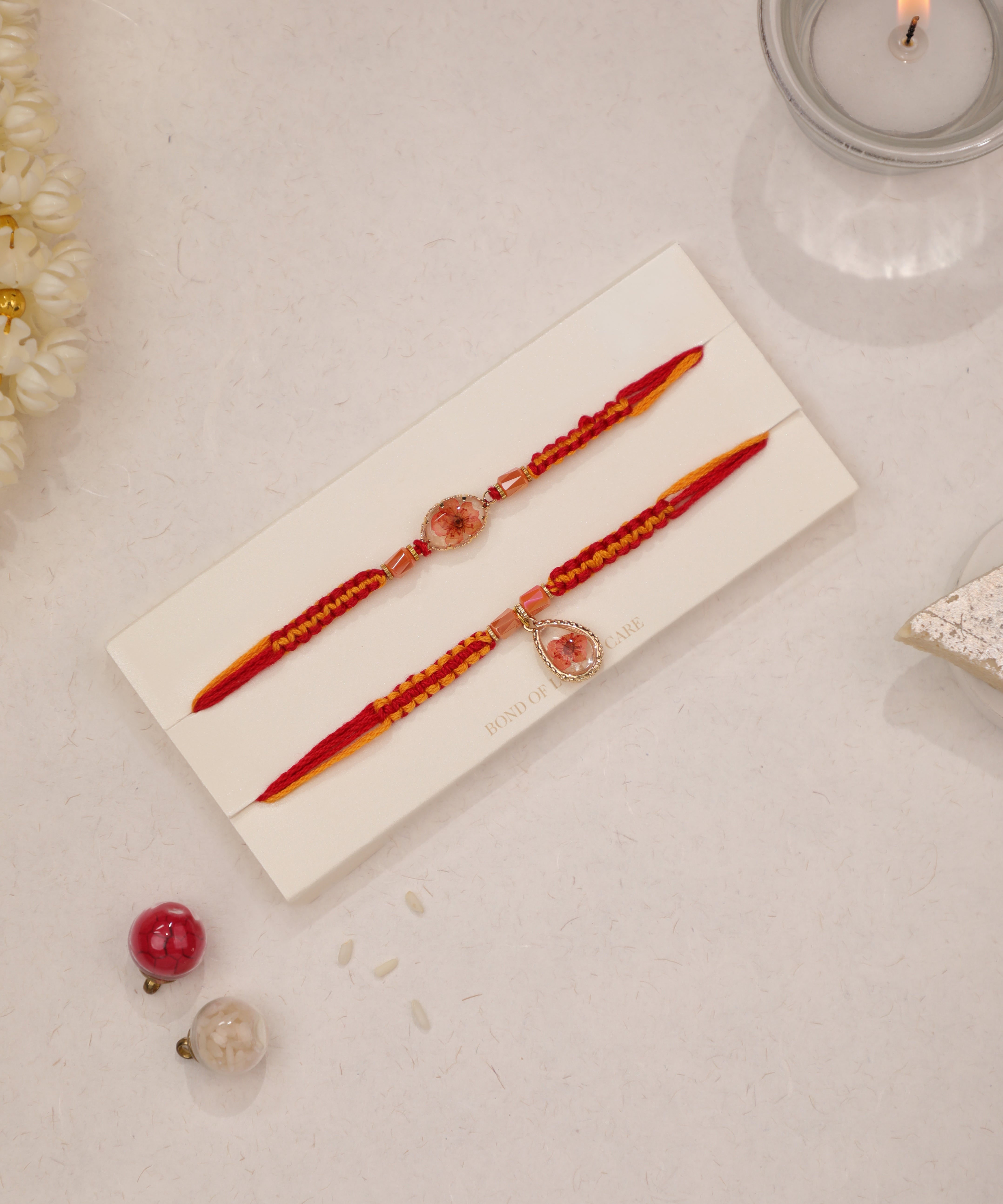 Gold-tone Rakhi set with preserved floral resin charms and red and yellow braided threads.