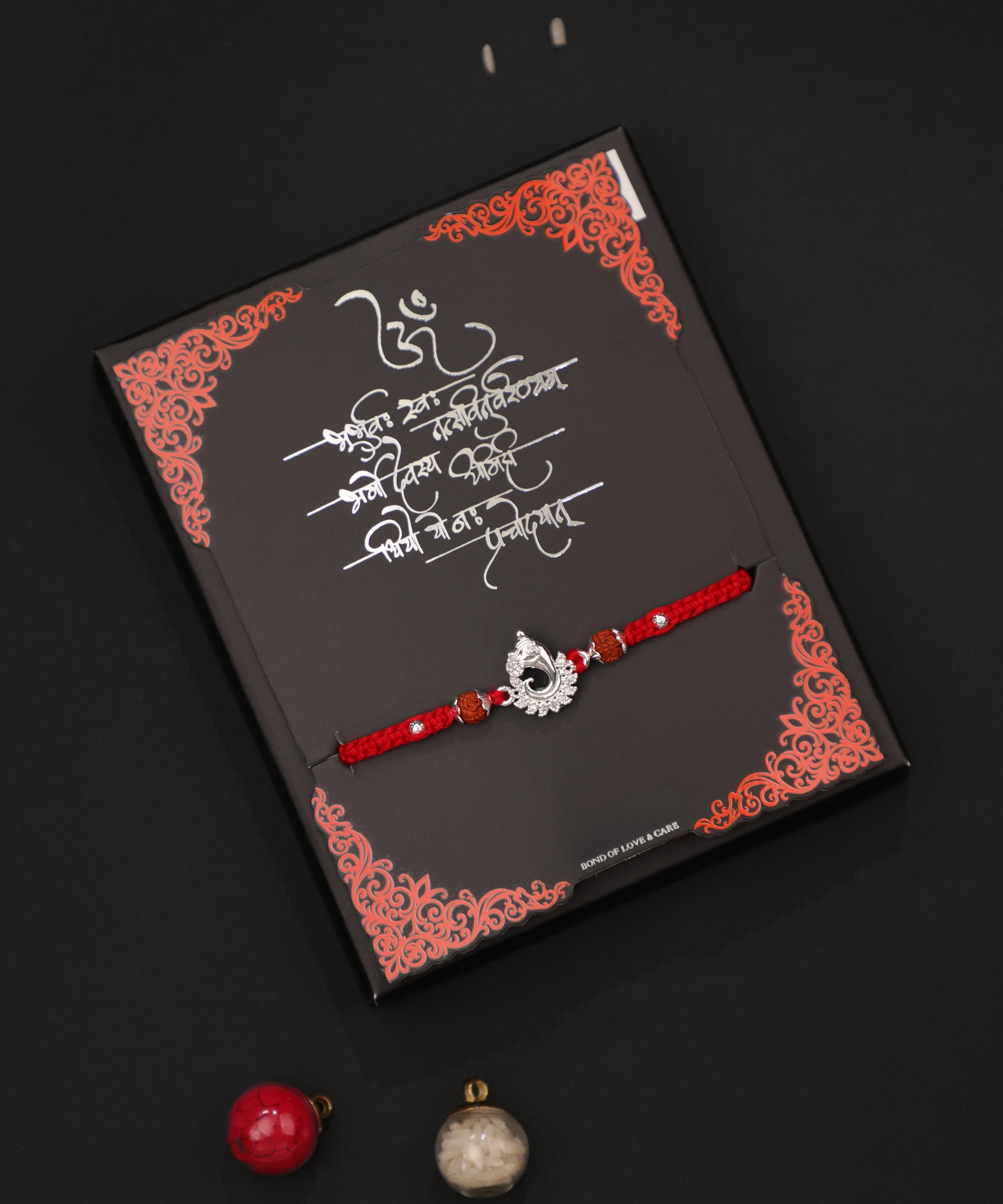 Rhodium finish Rakhi with intricate peacock design and clear stones on a red braided thread