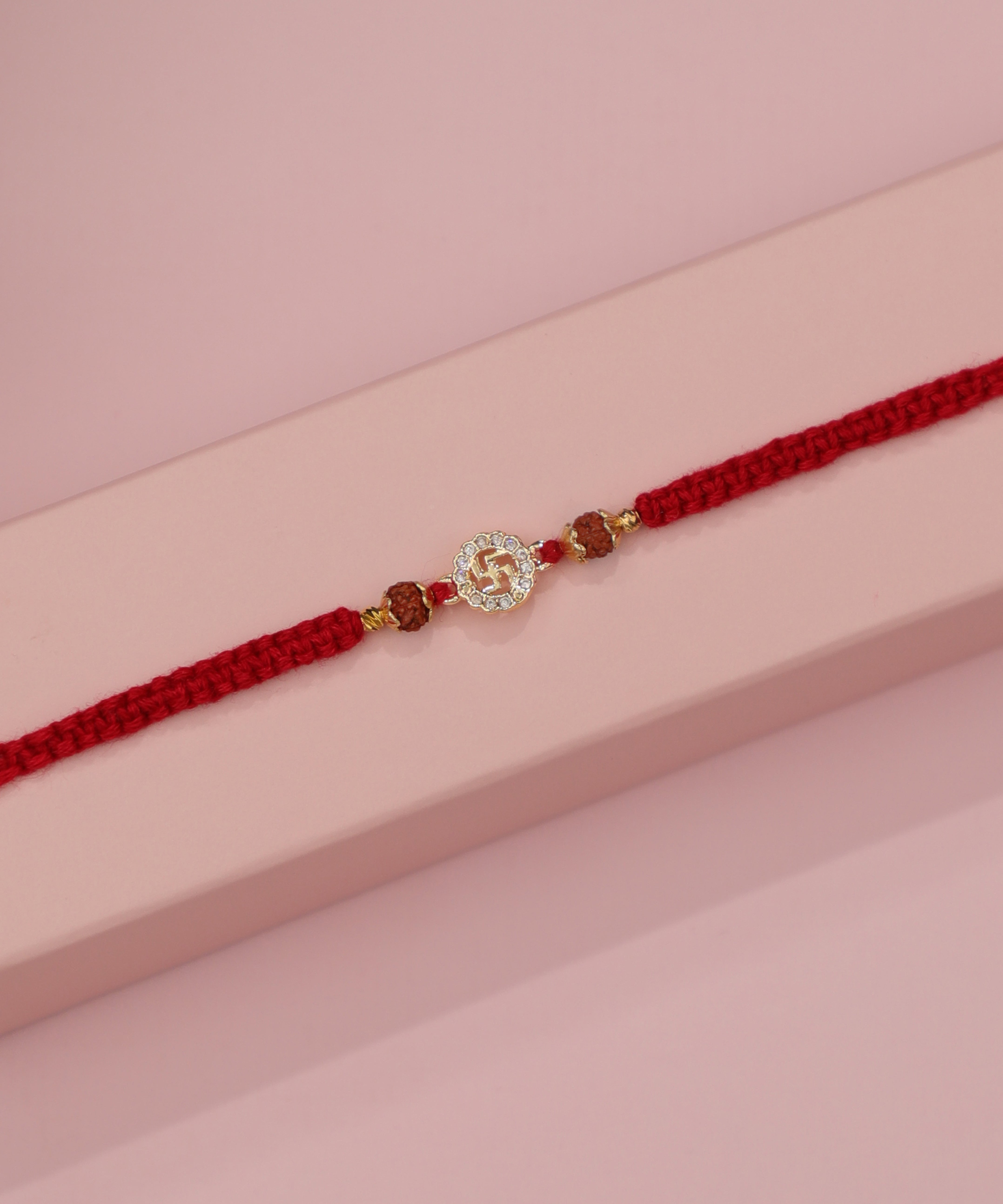 Gold-tone Rakhi with Swastika motif, clear stones, and brown beads on a red braided thread