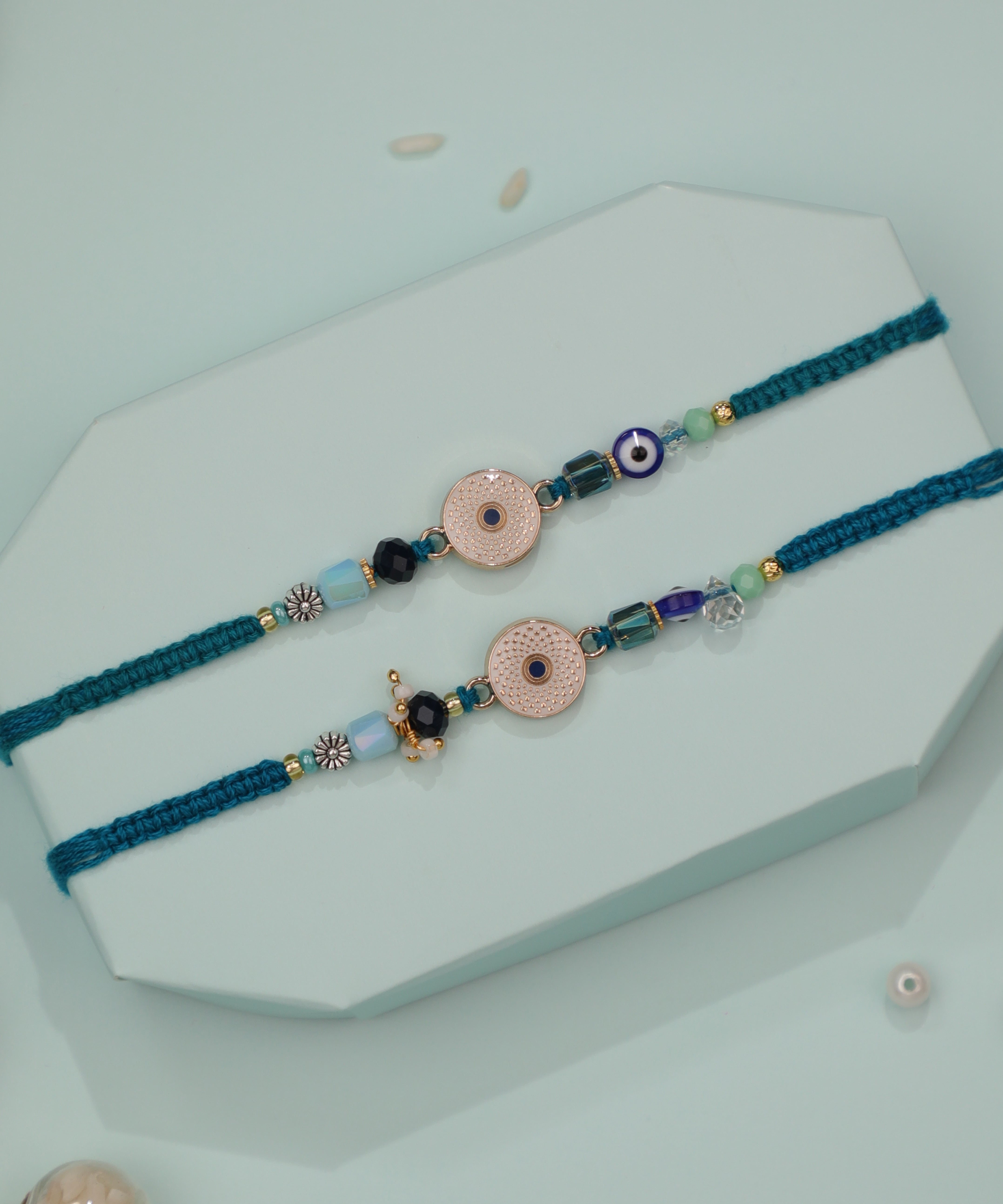Gold-tone Rakhi set with textured circular charms, evil eye and assorted glass beads on teal woven thread