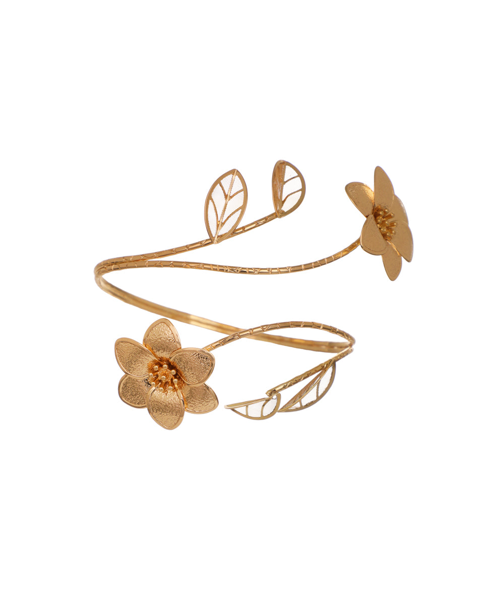 Gold-tone arm cuff with sculpted floral blossoms and filigree leaves on a winding vine design.