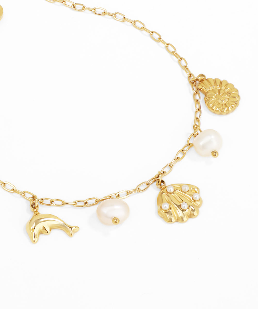 Gold bracelet with various charms including pearls and shell on a white background