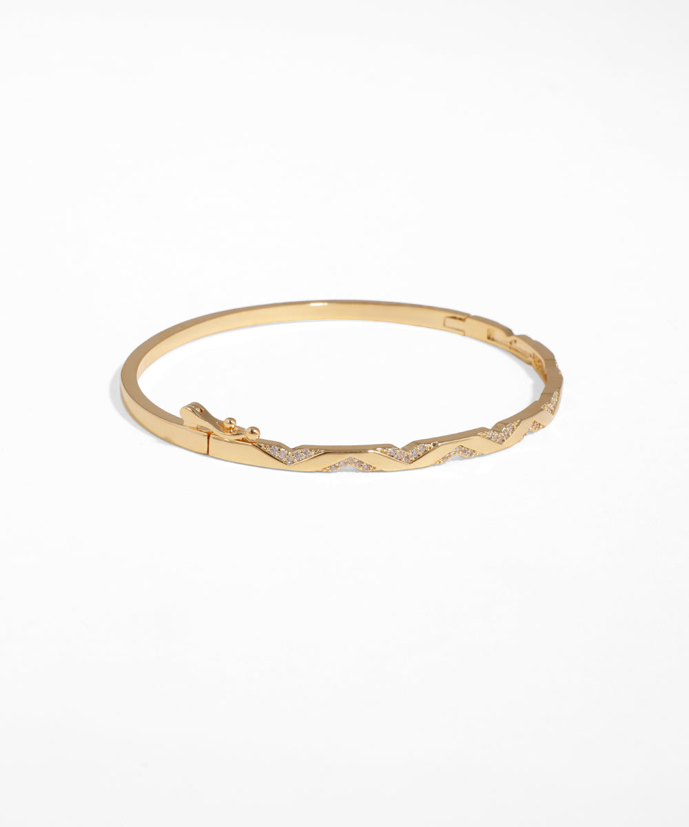 Gold bracelet with a wavy design on a white background