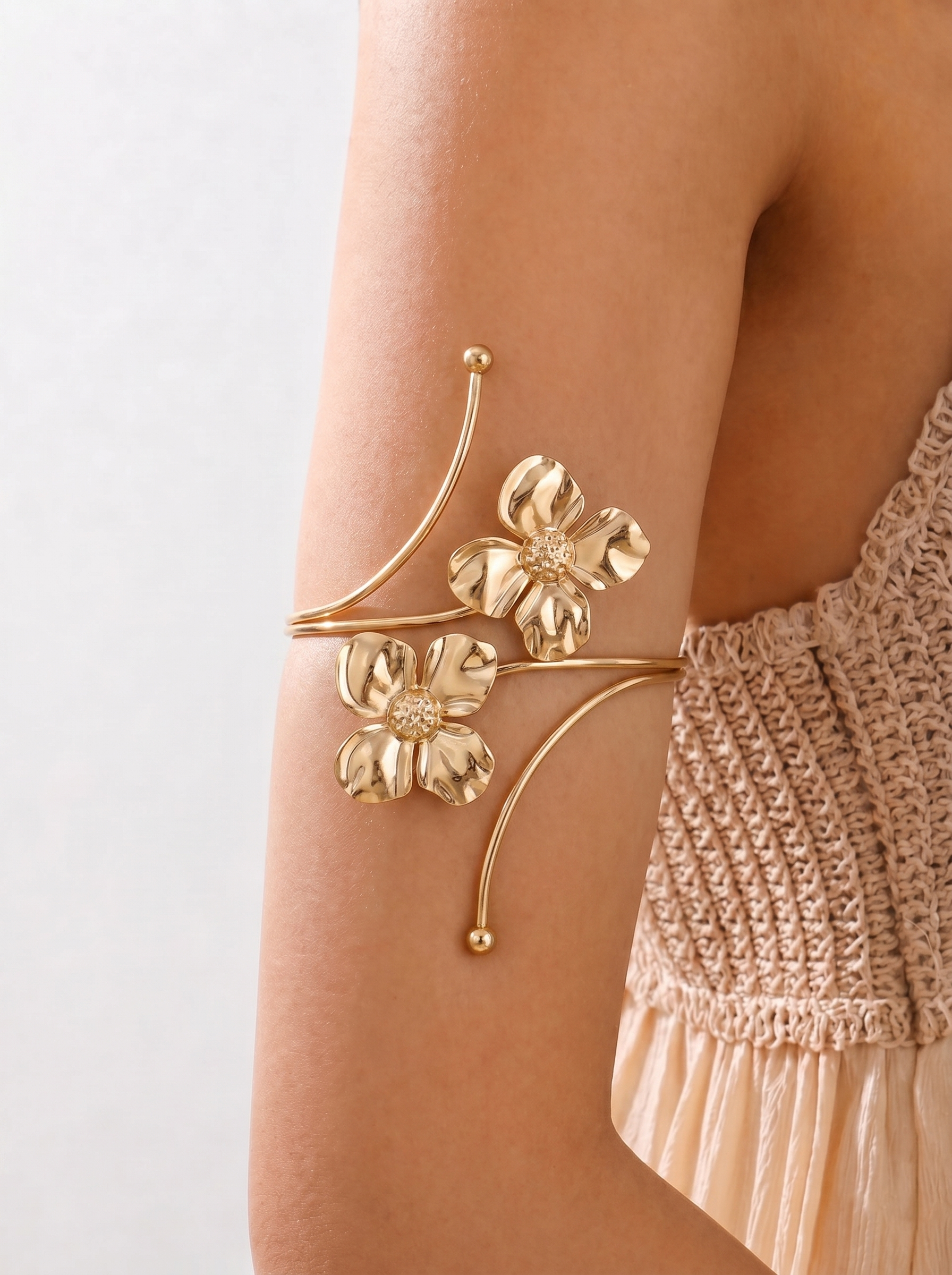 Gold floral arm cuff on a person's arm with a neutral background