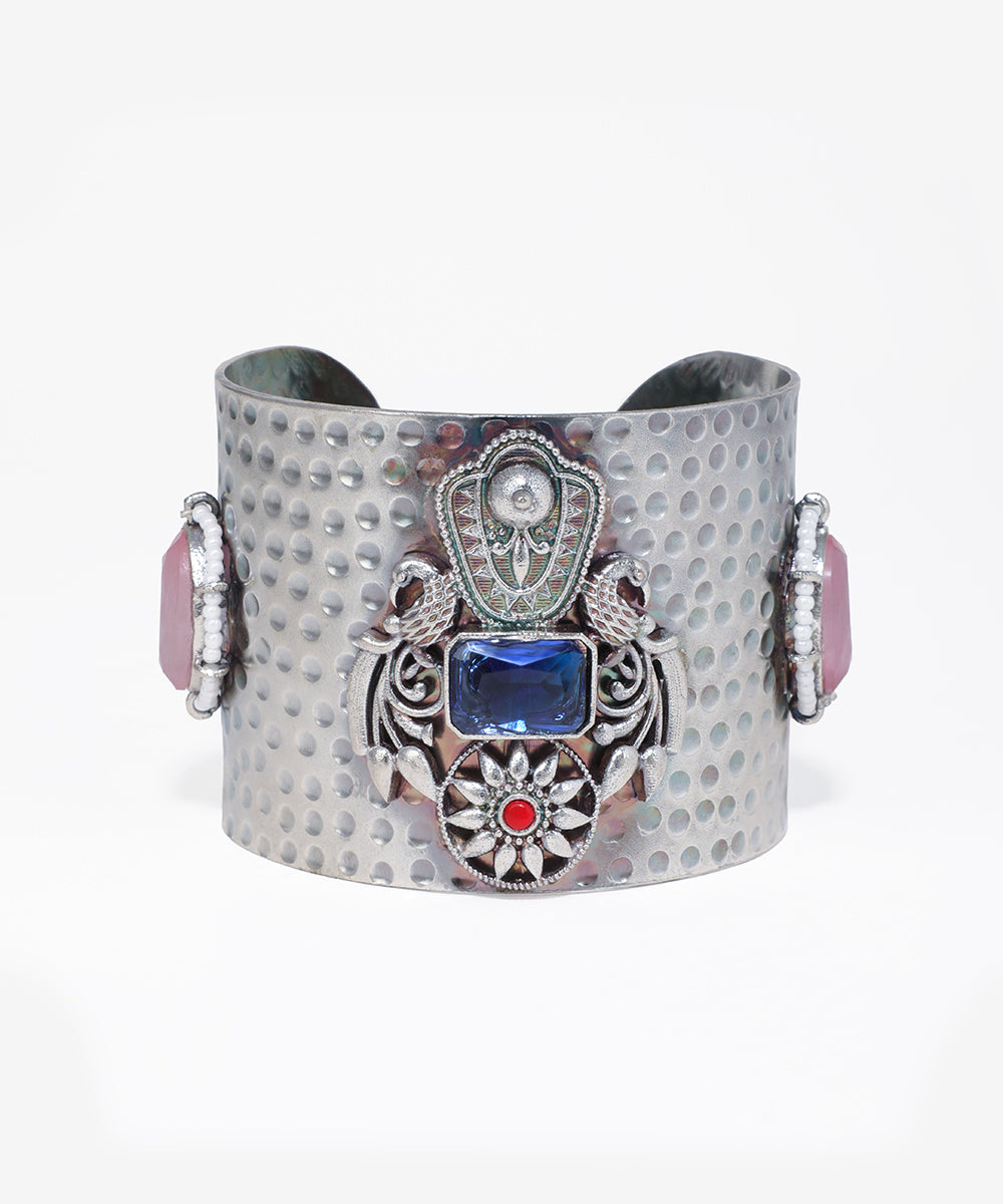 Decorative cuff bracelet with blue gemstone and intricate design on a white background