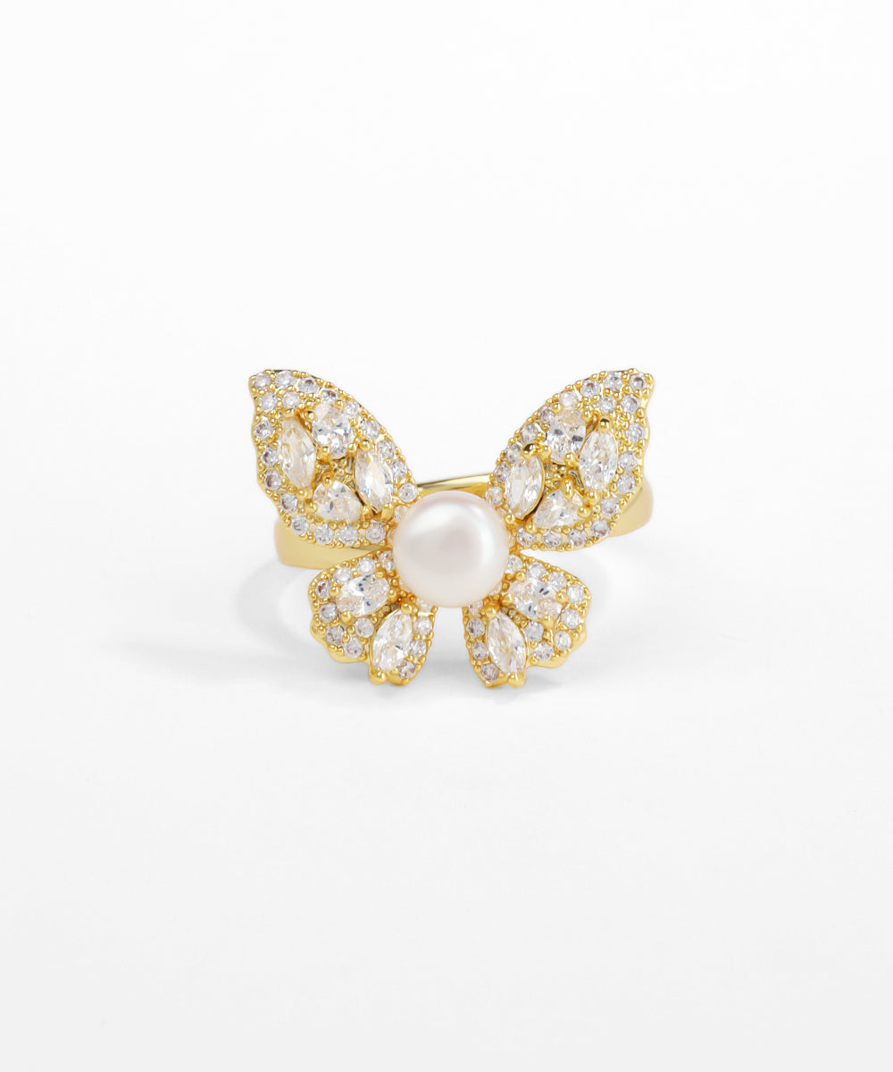 Gold butterfly-shaped ring with a pearl center on a white background