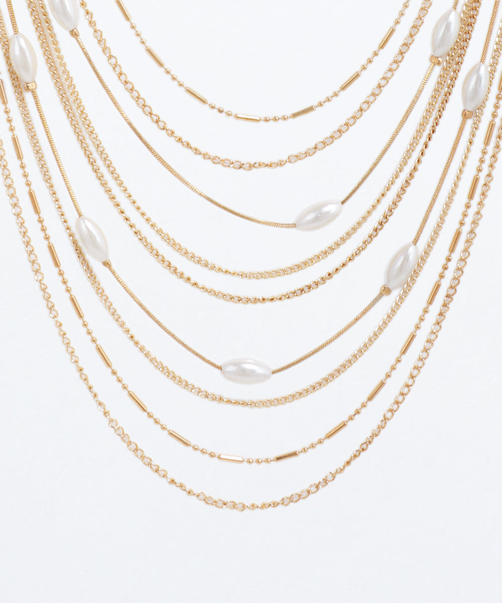 Gold chain necklace with white beads on a light gray background