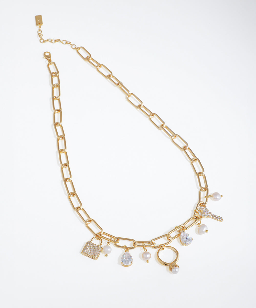 Gold-tone necklace with paperclip chain and assorted charms including lock, key, ring, CZ, and faux pearls.