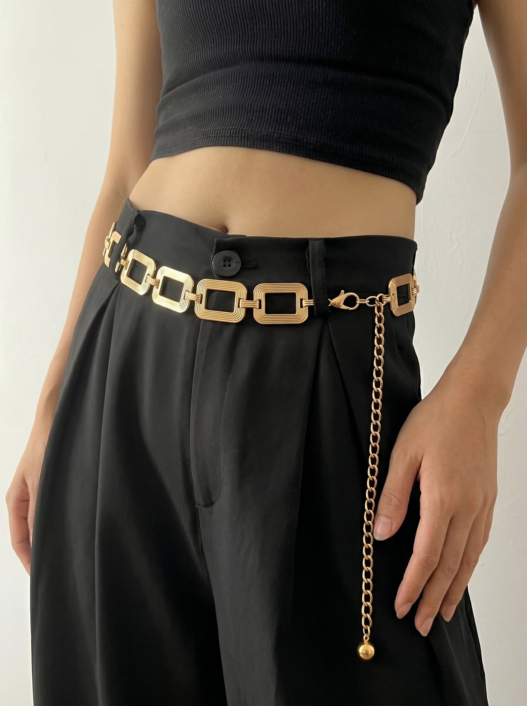 Person wearing a black outfit with a gold chain belt on a plain background