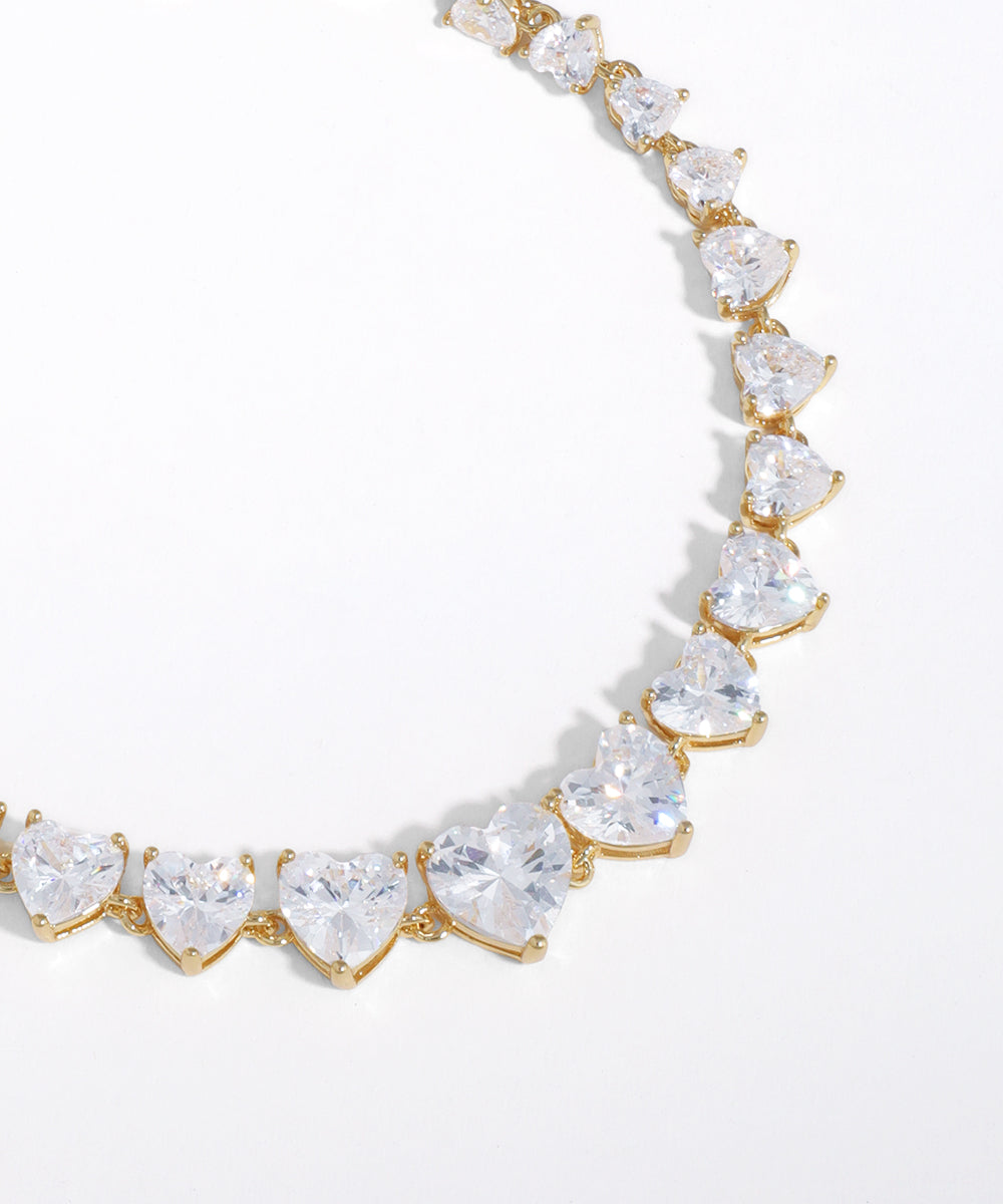 Gold necklace with heart-shaped clear gemstones on a white background