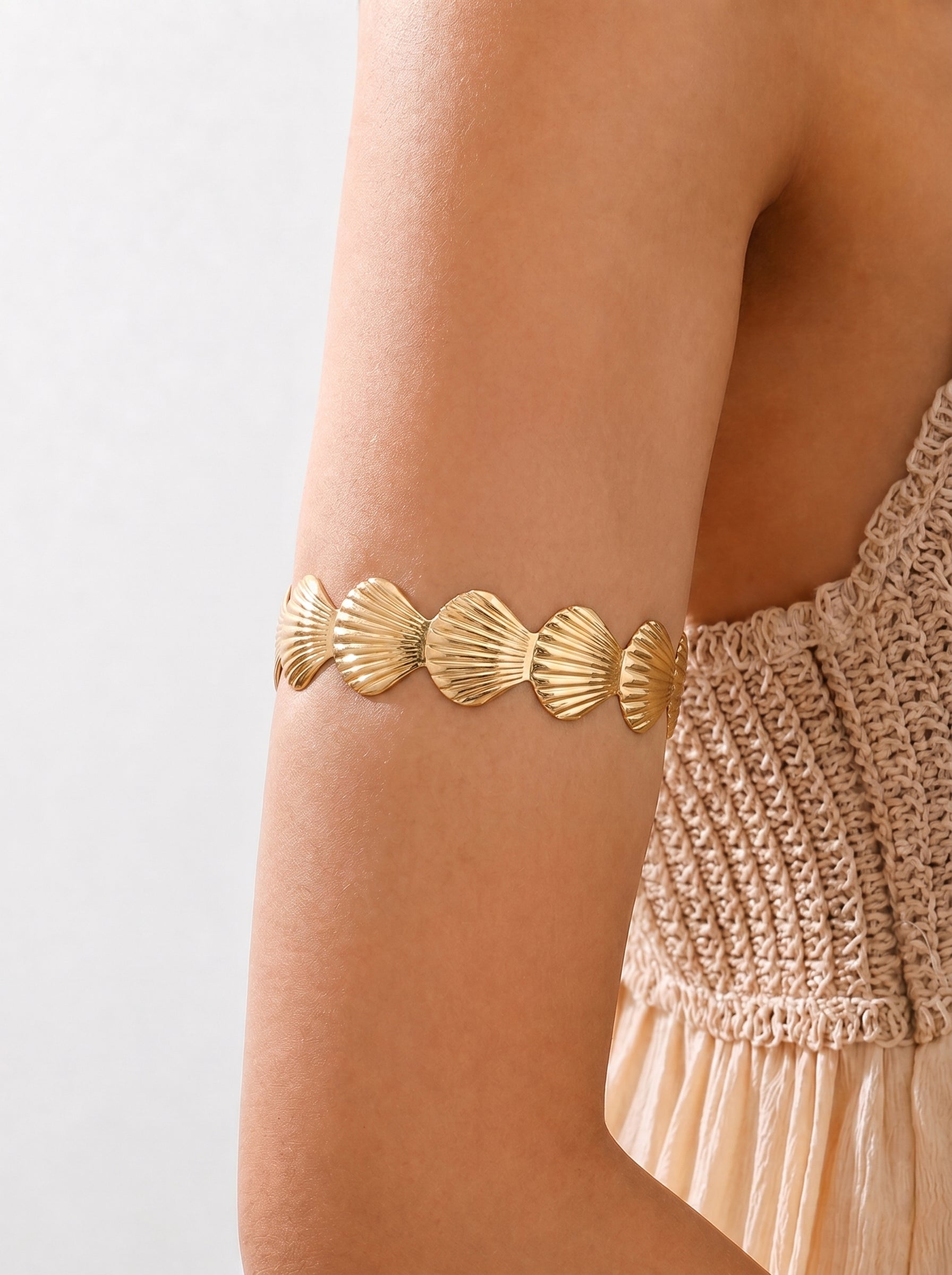 Gold shell-patterned bracelet on a person's wrist with a neutral background