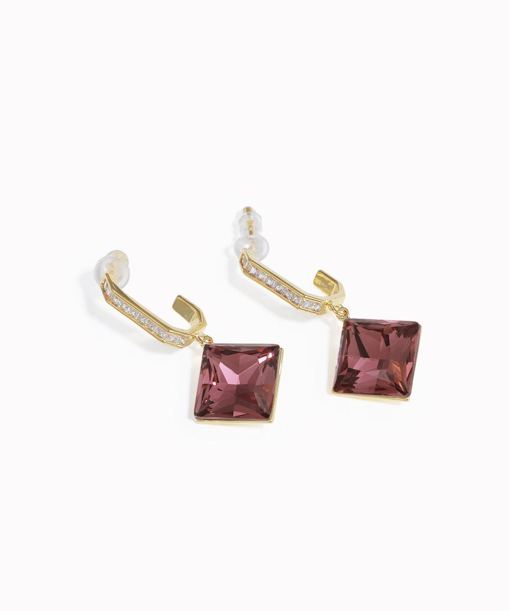 Gold earrings with pink square gemstones on a white background