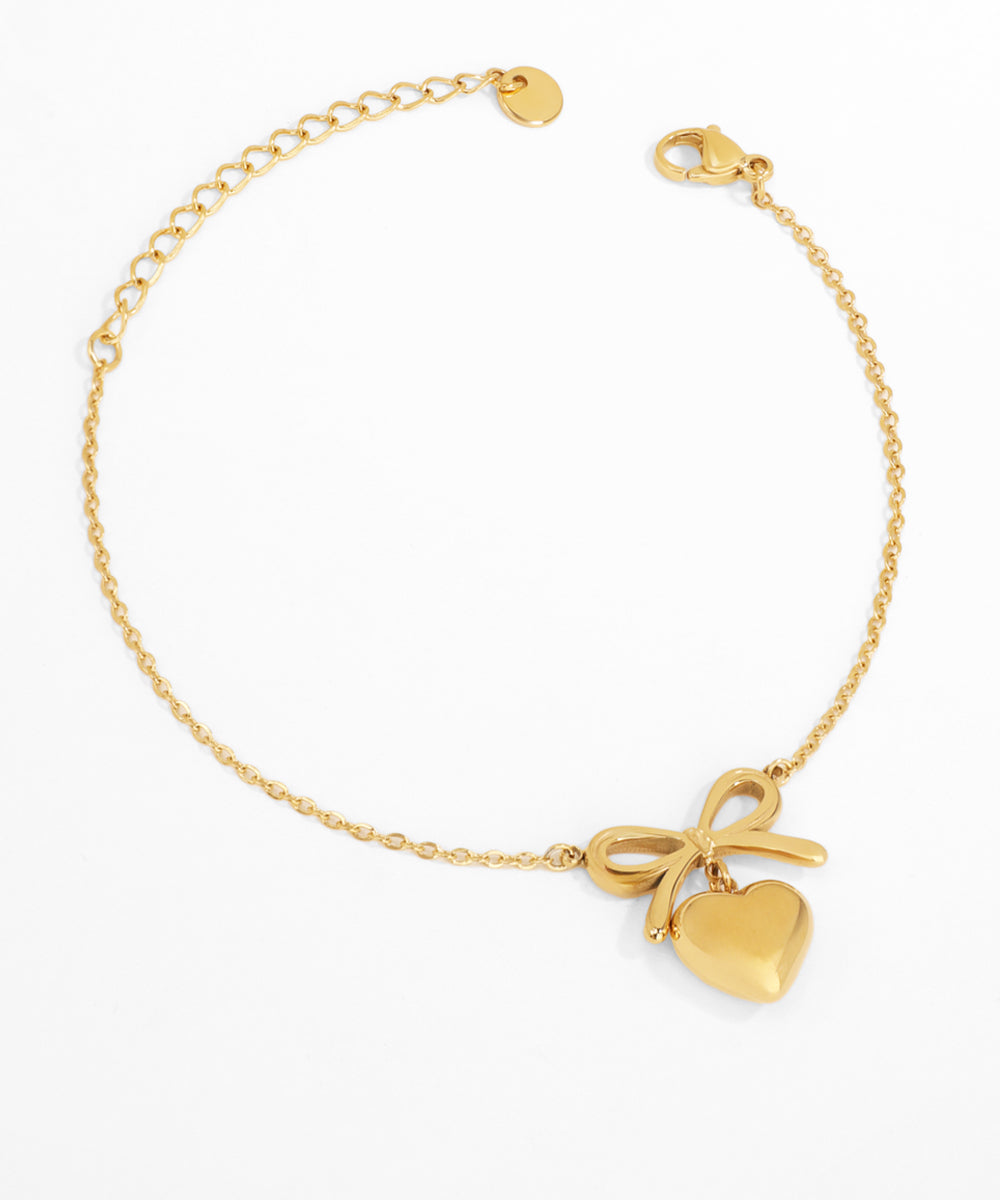Gold bracelet with heart and bow charm on a white background