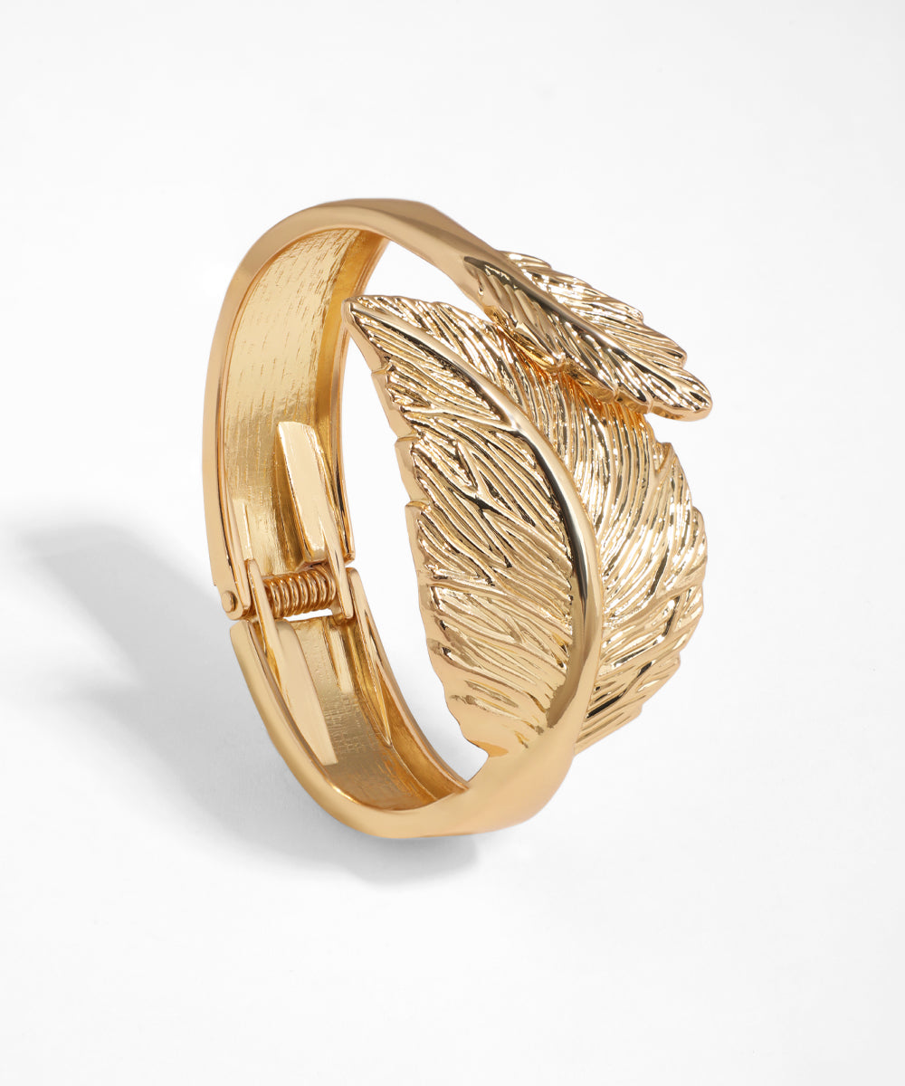 Gold-tone bangle bracelet with intricate embossed feather motifs and hinge closure.