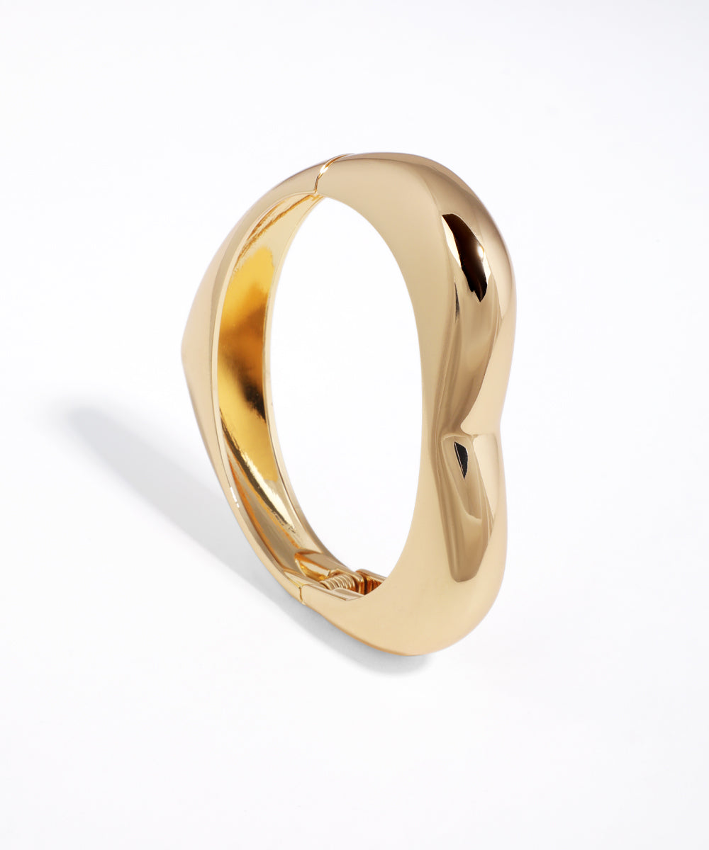 Shiny gold-tone cuff bracelet with a modern sculptural wavy design and hinge closure
