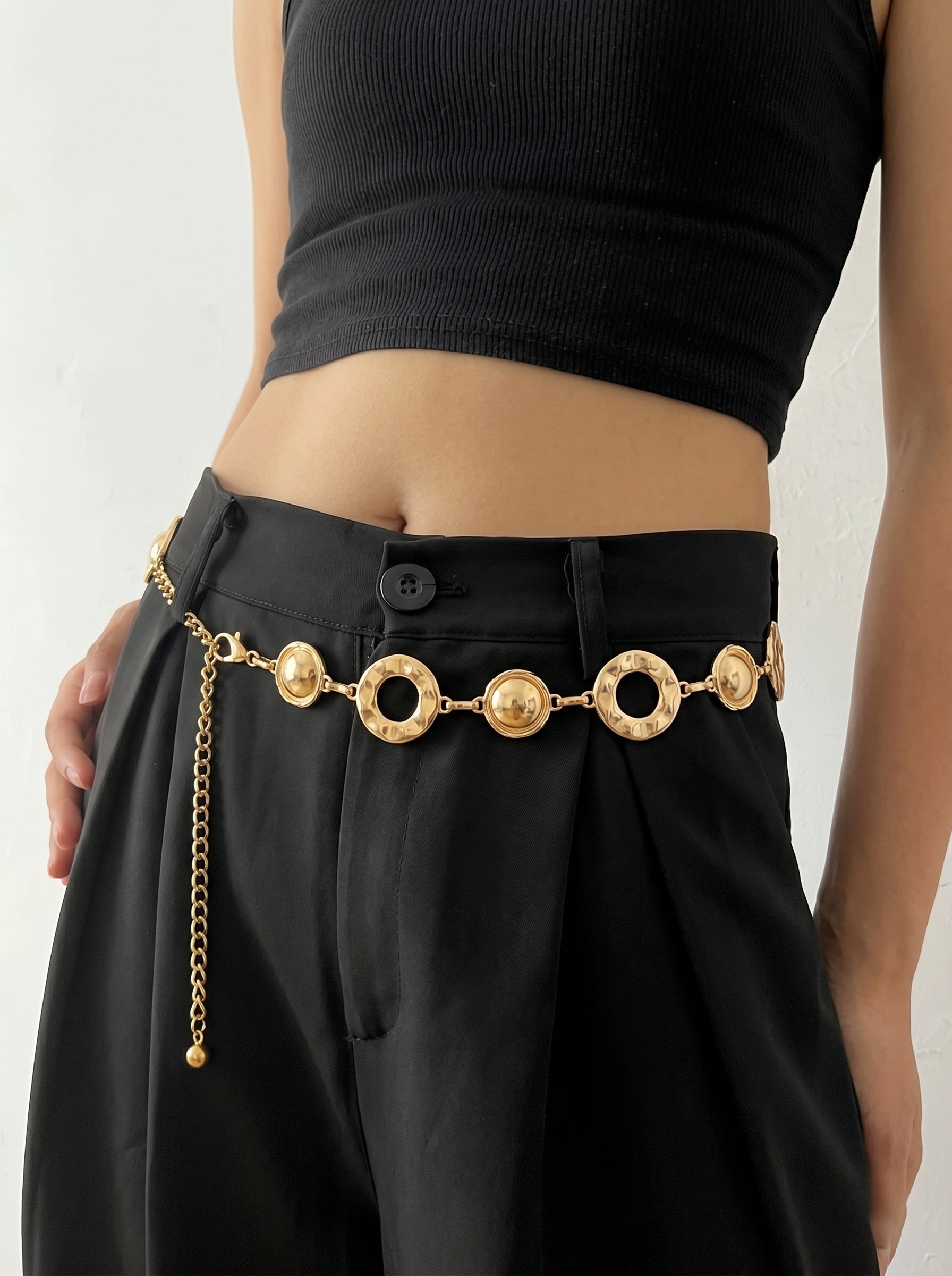 Person wearing a black outfit with a gold belt featuring circular designs on a plain background