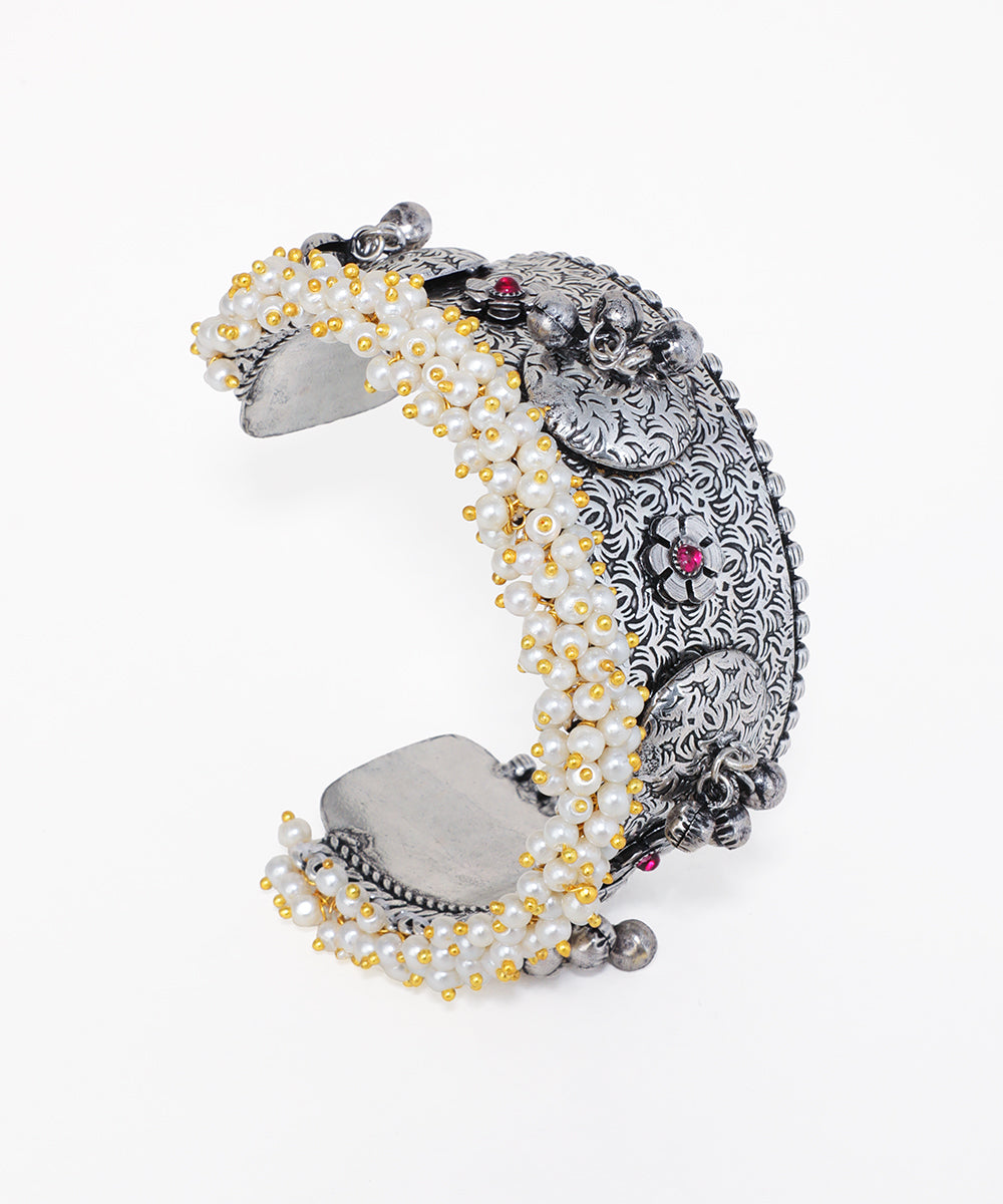 Oxidised silver-tone cuff bracelet with intricate floral patterns, faux pearls, and red glass crystals.
