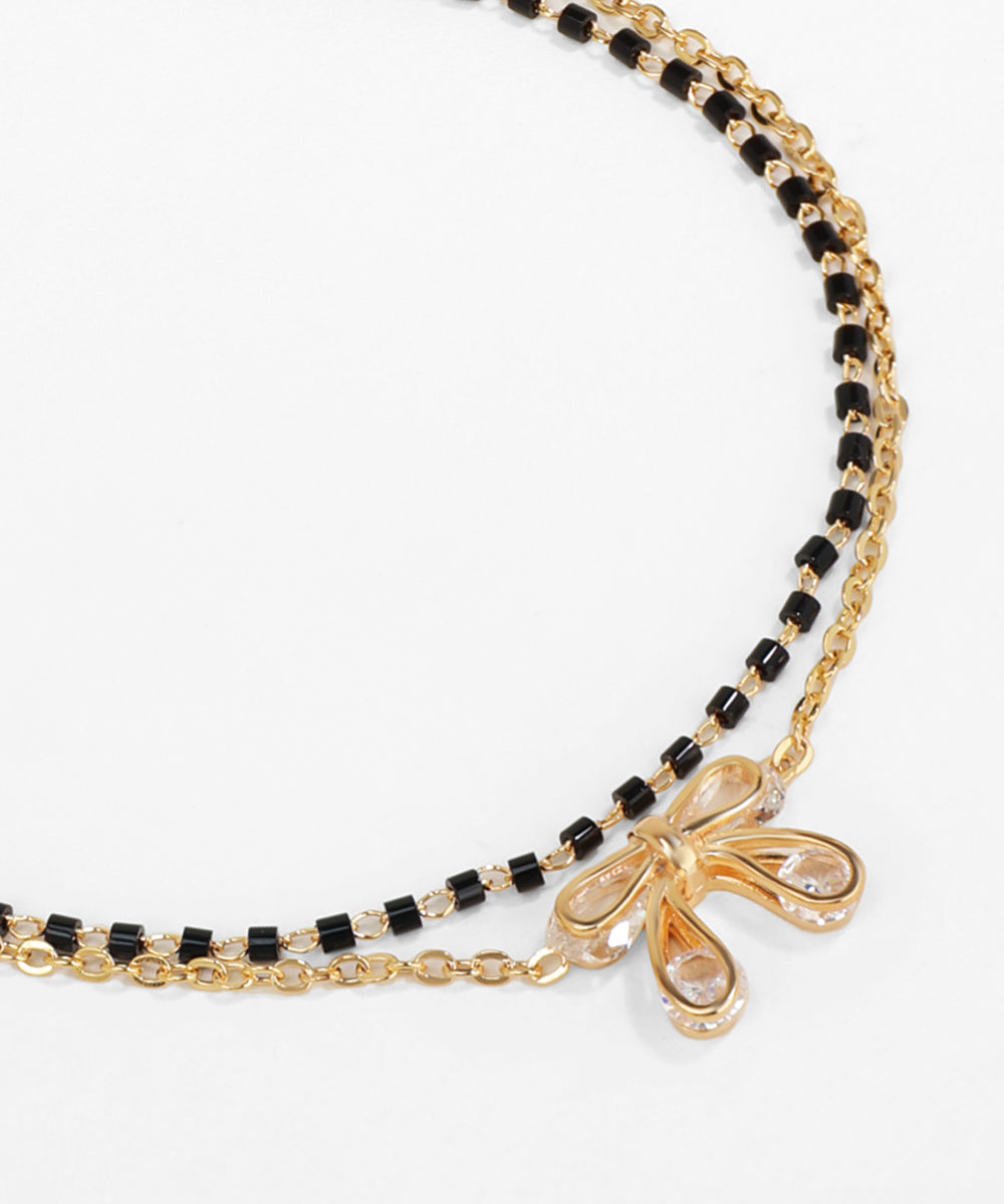Gold and black beaded necklace with a bow pendant on a white background