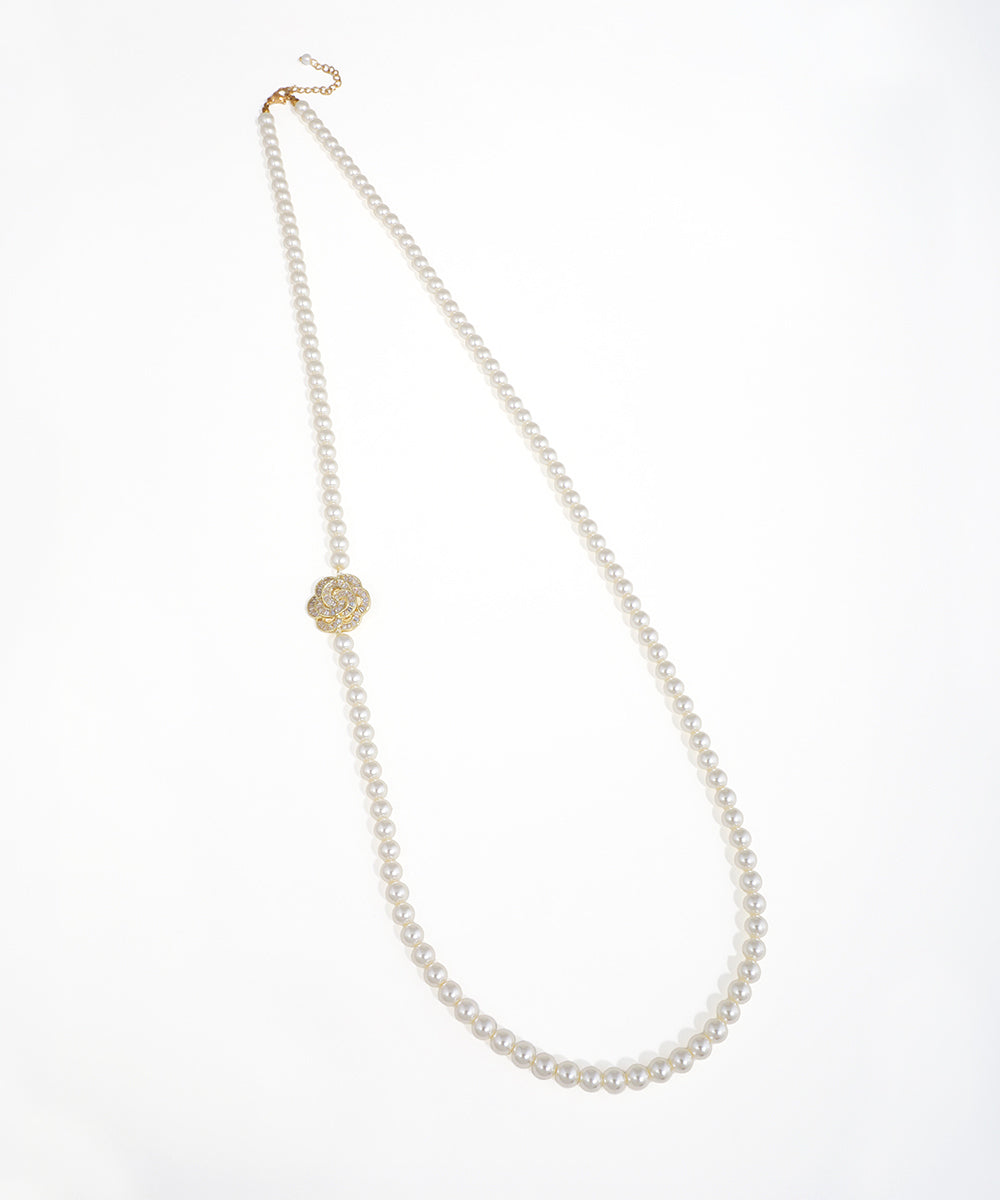 Gold-tone long beaded necklace with an off-center floral accent adorned with clear stones