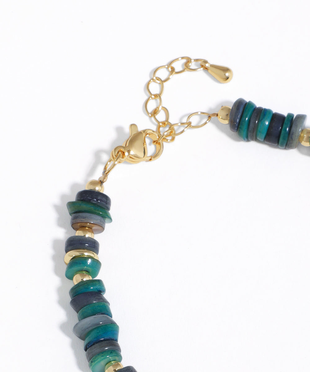 Bracelet with green and gold beads on a white background