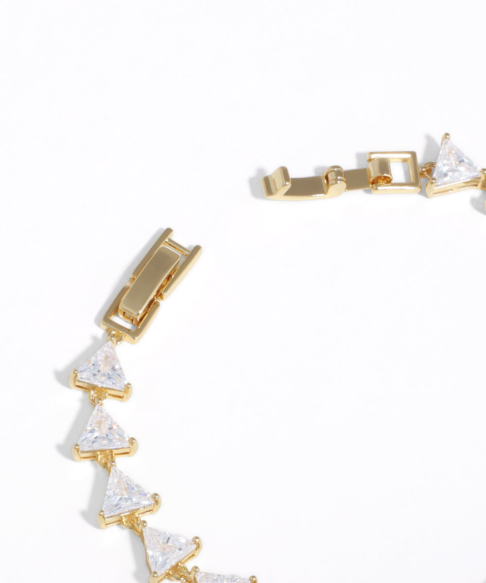 Gold bracelet with clear triangular stones on a white background