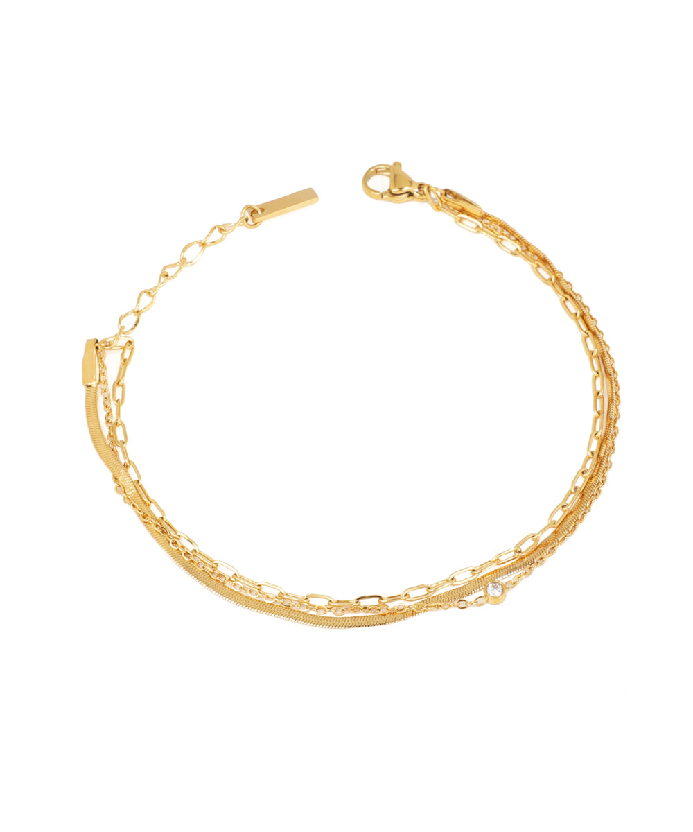 Gold-tone layered bracelet with mixed chain links and a single clear cubic zirconia stone