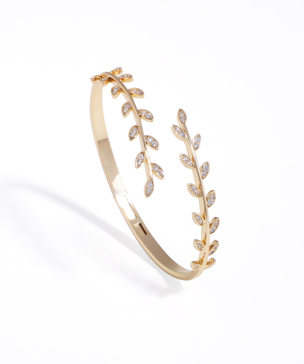 Gold-tone bracelet with sparkling leaf vine design and hinge closure.