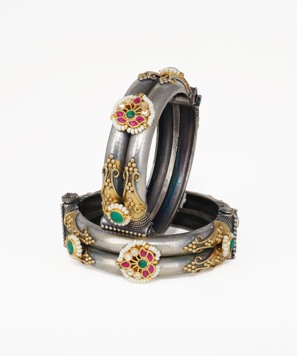 Set of ornate bangles with floral designs and gemstones on a white background