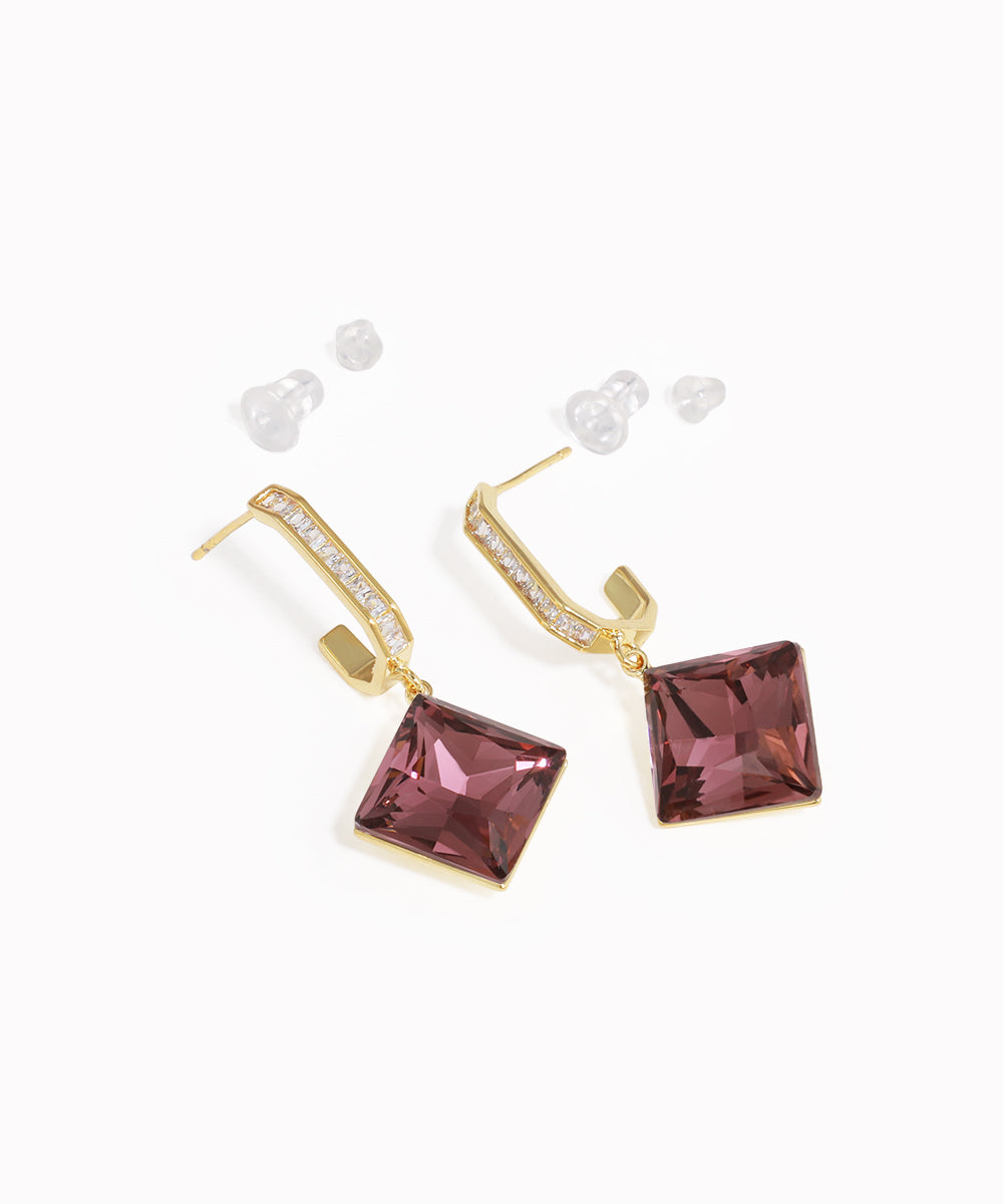 Gold earrings with purple gemstones on a white background