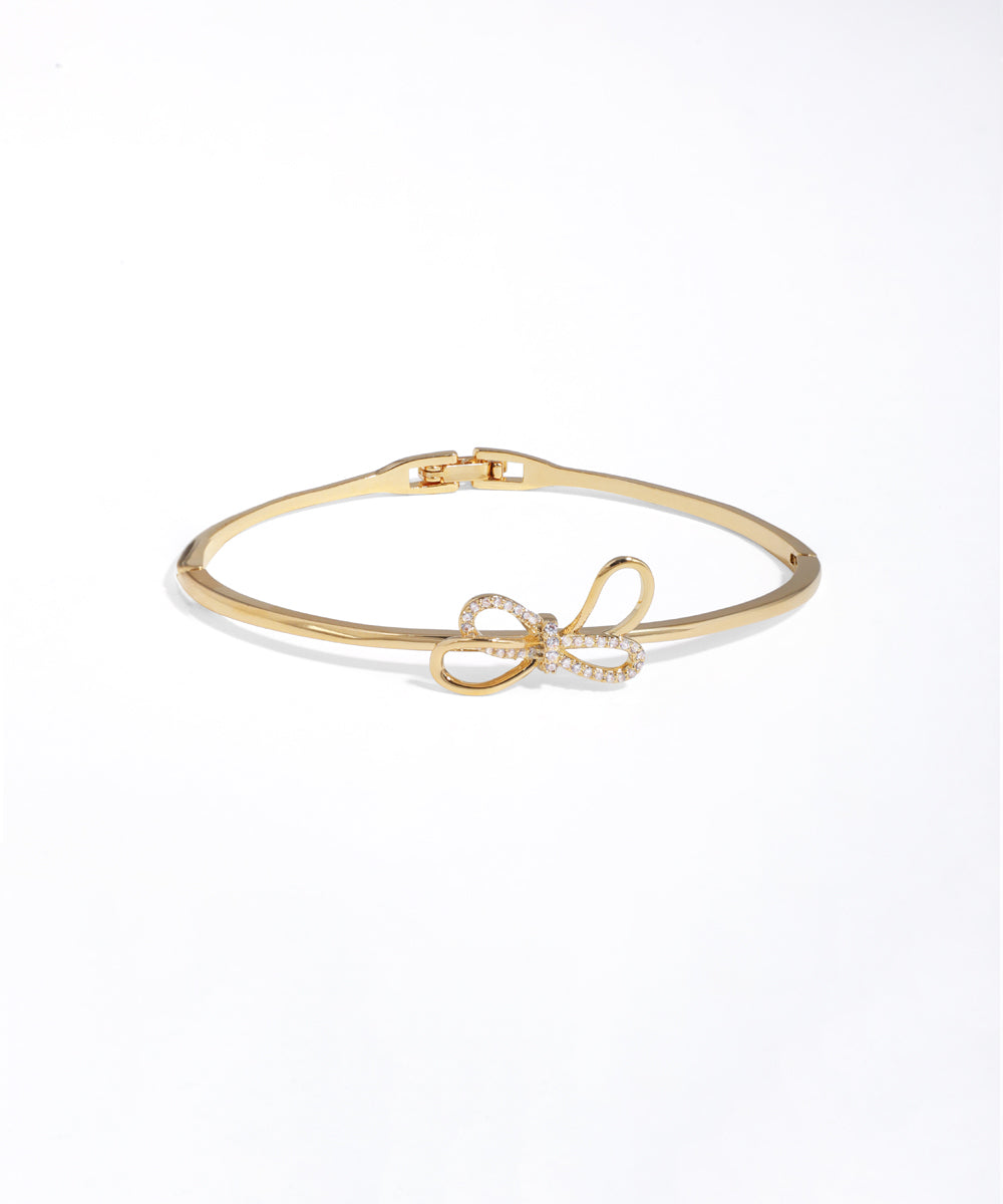 Gold bracelet with a bow charm on a white background