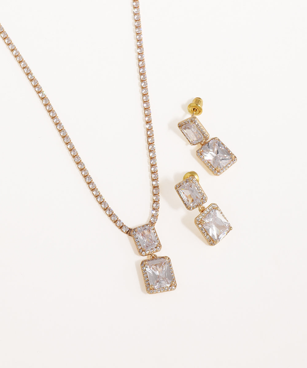 Gold necklace and earrings with clear gemstones on a white background