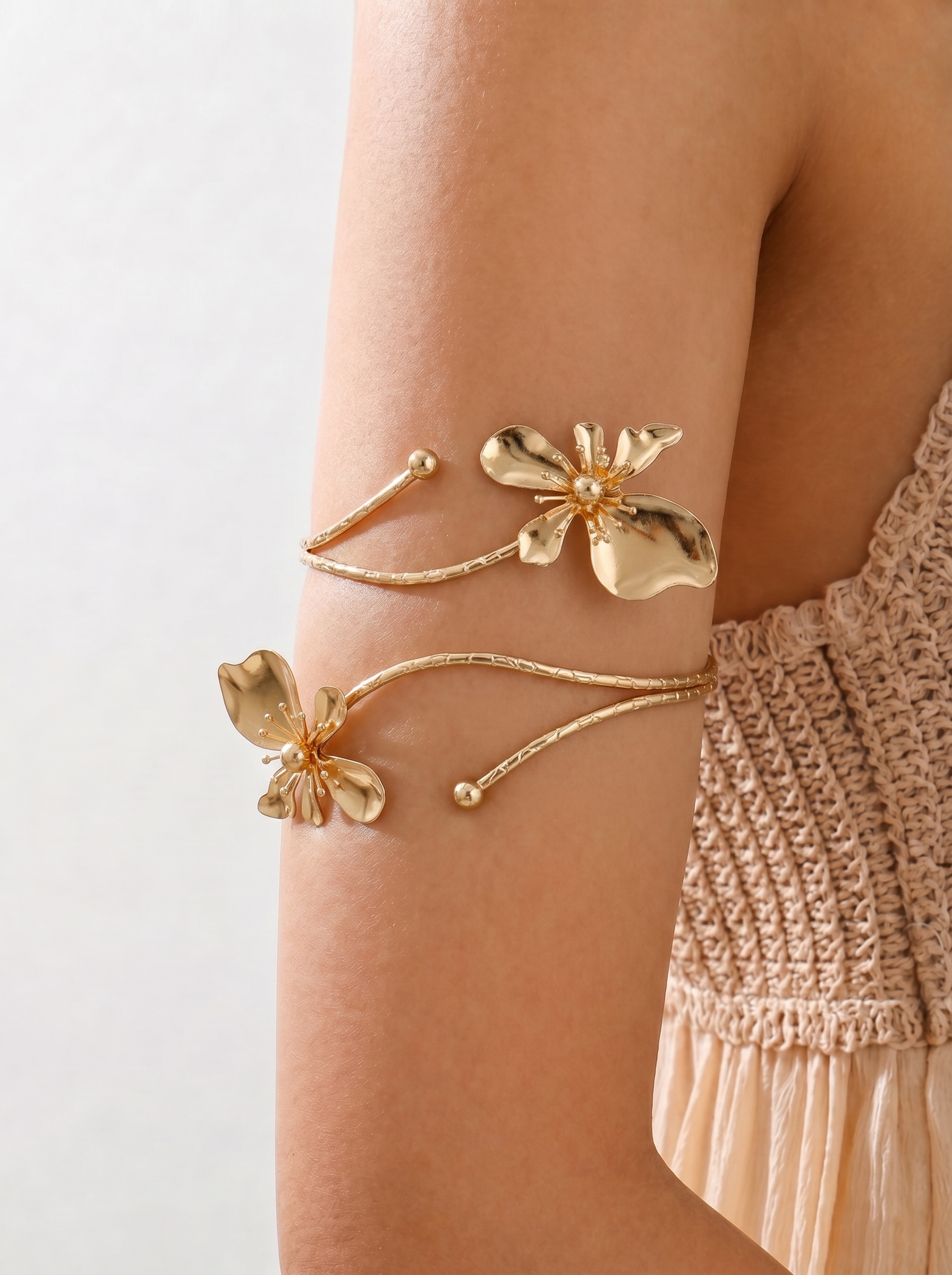 Gold floral arm cuffs on a person's arm with a neutral background