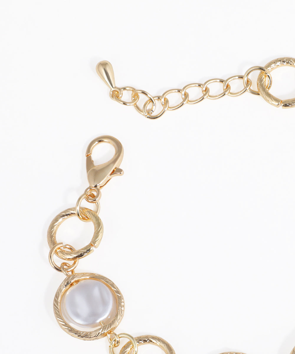 Gold bracelet with a pearl-like center on a white background