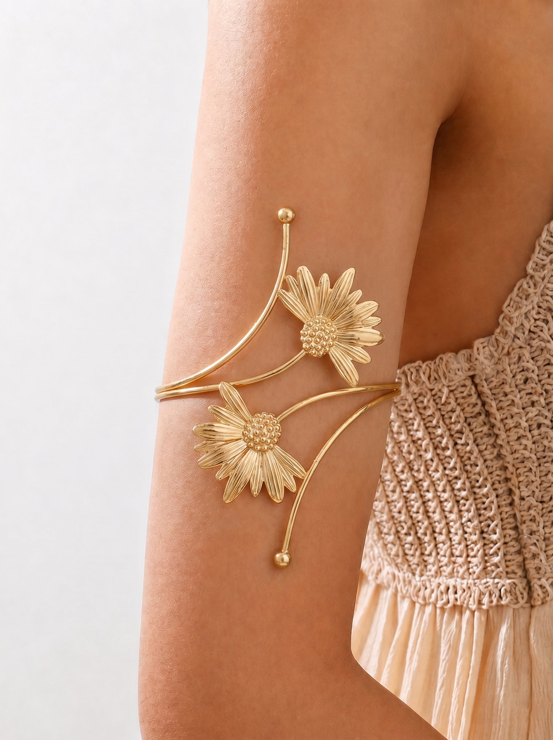 Gold floral arm cuff on a person's arm with a neutral background