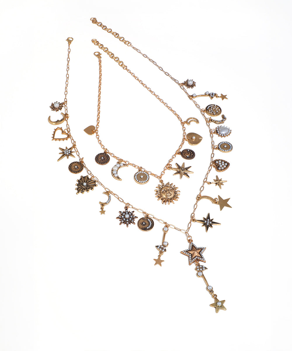 Gold-tone layered necklace with various celestial and heart charms, featuring faux pearls and small clear stones.