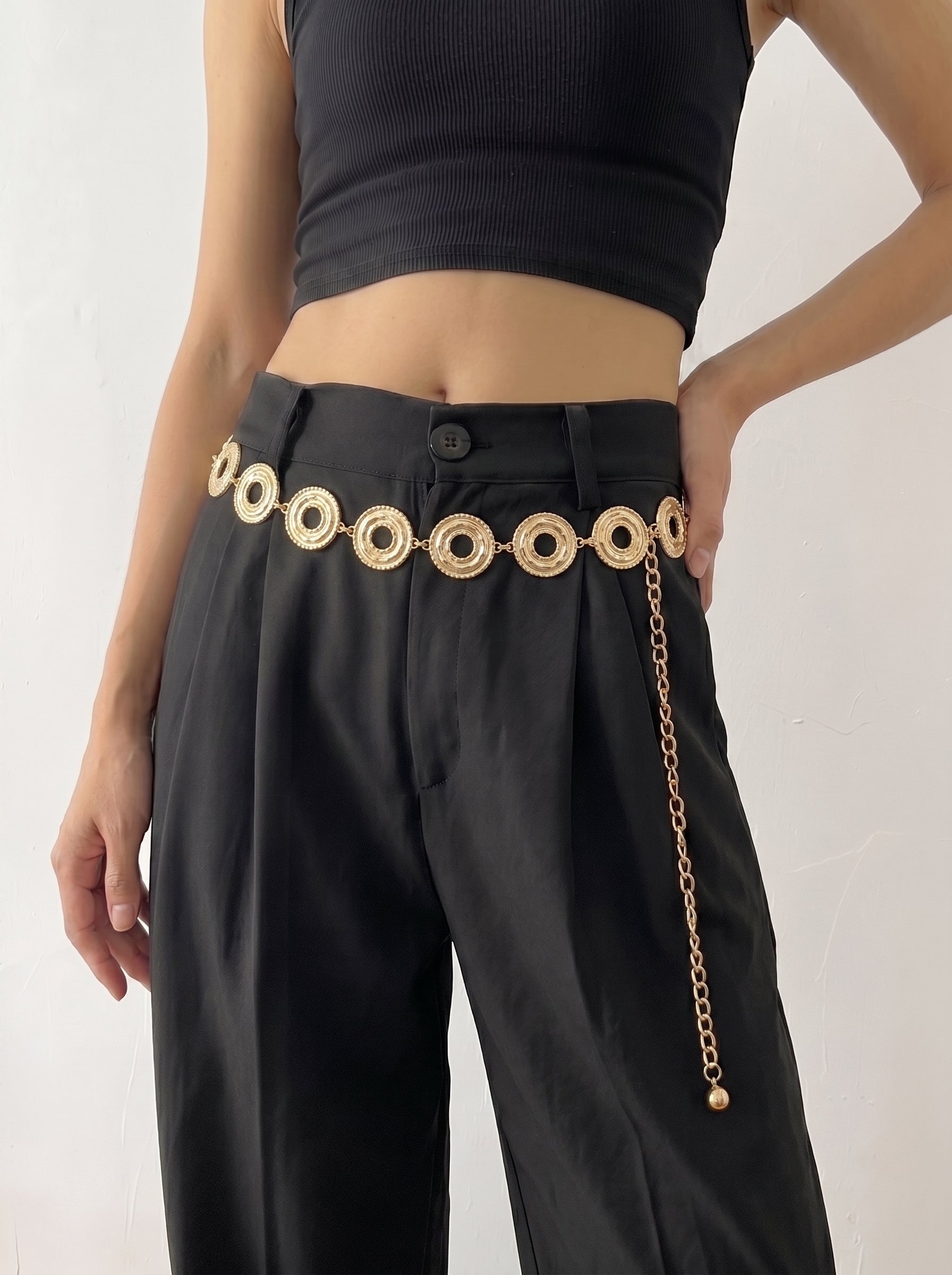 Person wearing black pants with a gold belt and chain on a white background
