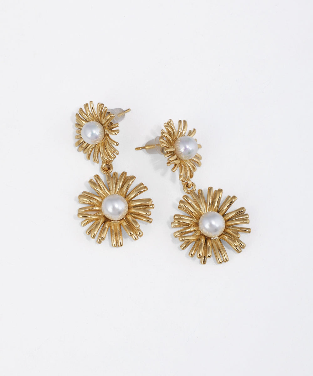 Gold-tone drop earrings with textured floral sunburst design and central faux pearls on white background.