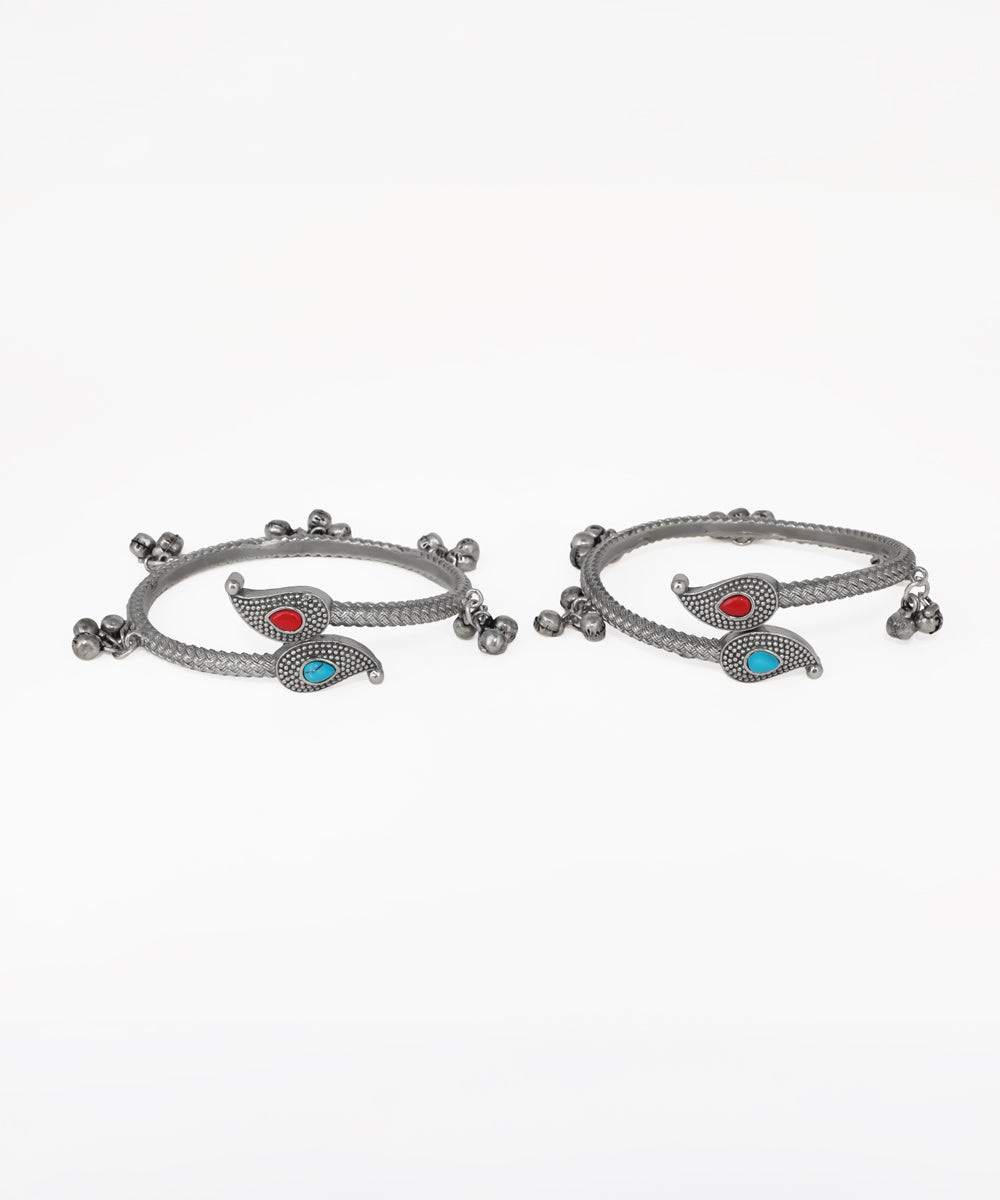Pair of silver bangles with red and blue stones on a white background