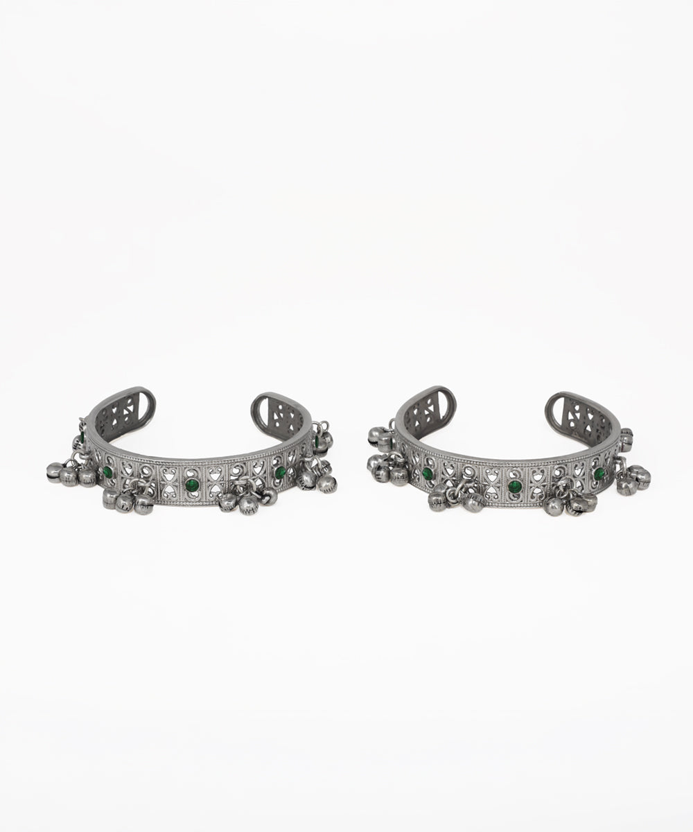 Pair of silver cuff bracelets with green gemstones on a white background