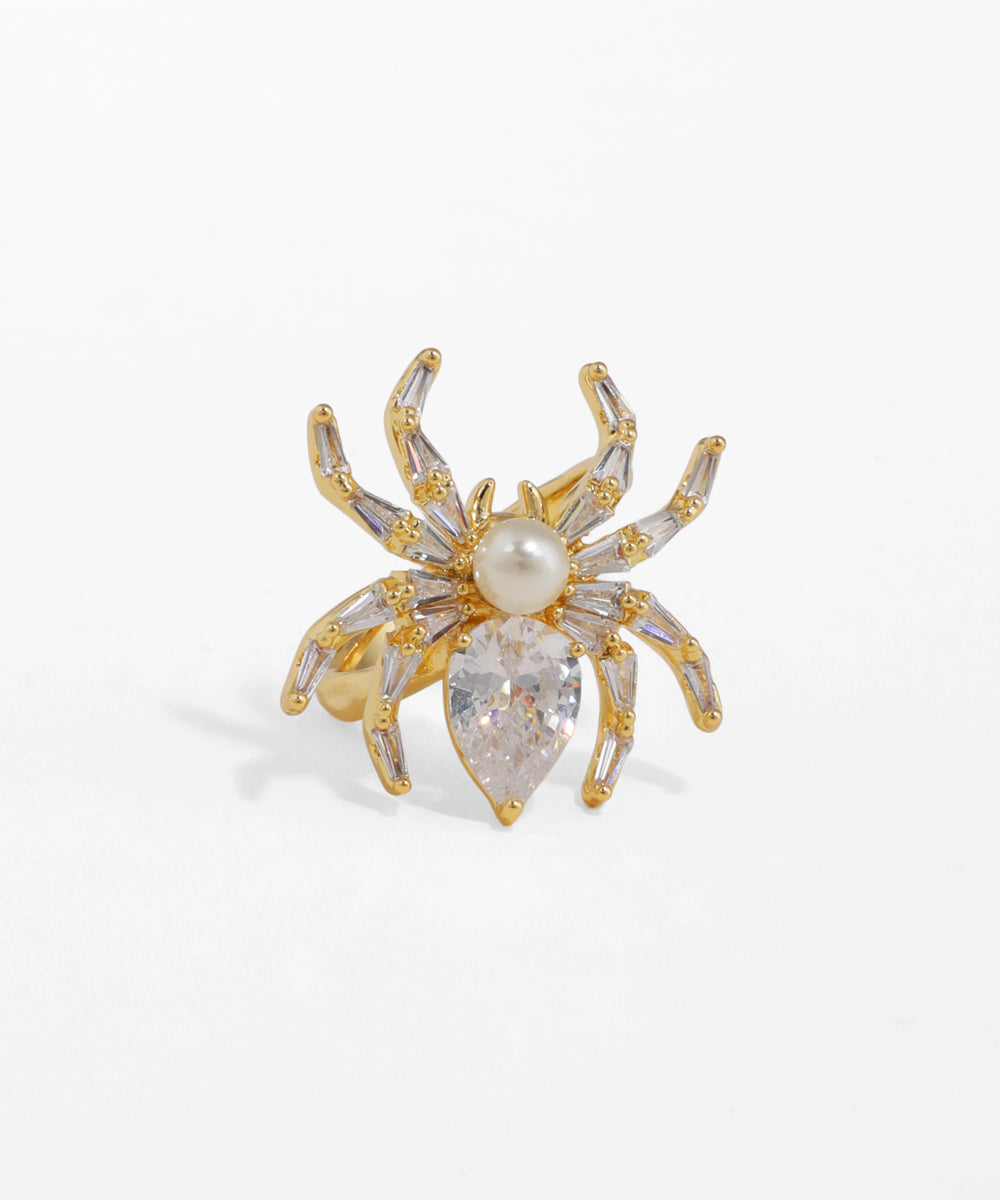 Gold-tone ring with a detailed spider motif, featuring a pear-shaped clear stone body and faux pearl head.