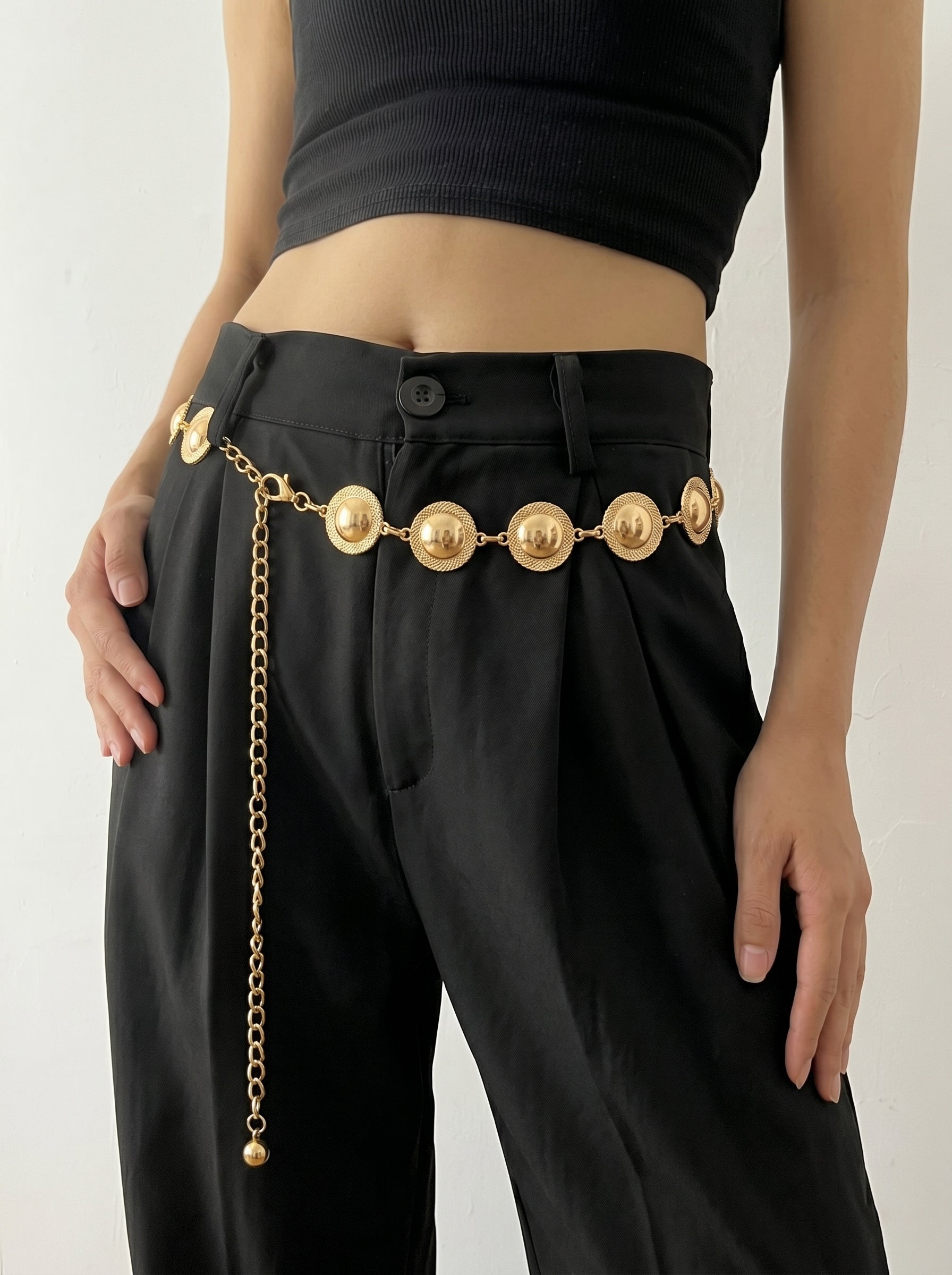 Person wearing black pants with a gold chain belt on a plain background