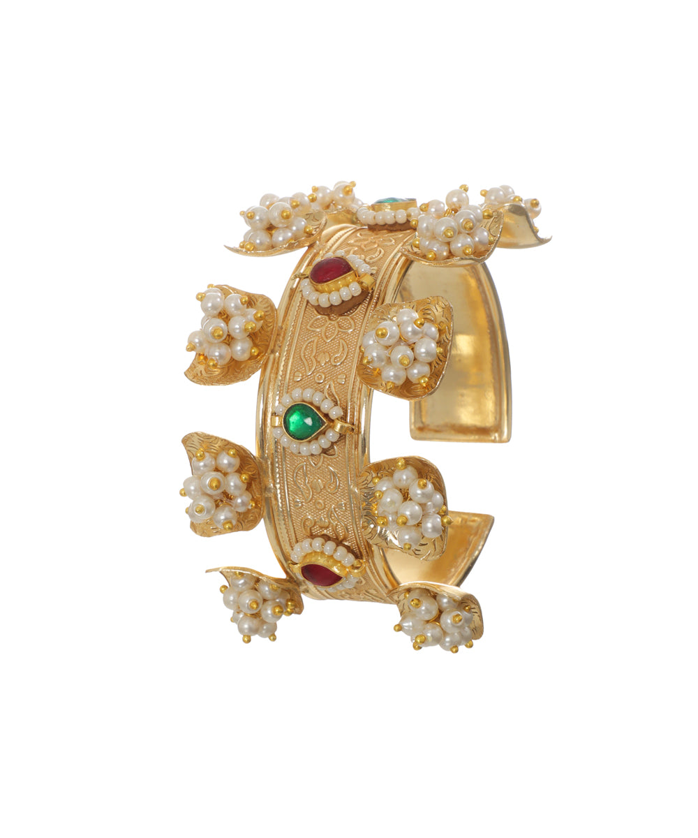 Gold-tone cuff bracelet with intricate engraving, pearl clusters, and red and green glass stones.