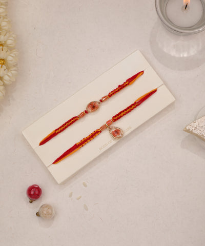 Gold-tone Rakhi set with preserved floral resin charms and red and yellow braided threads.