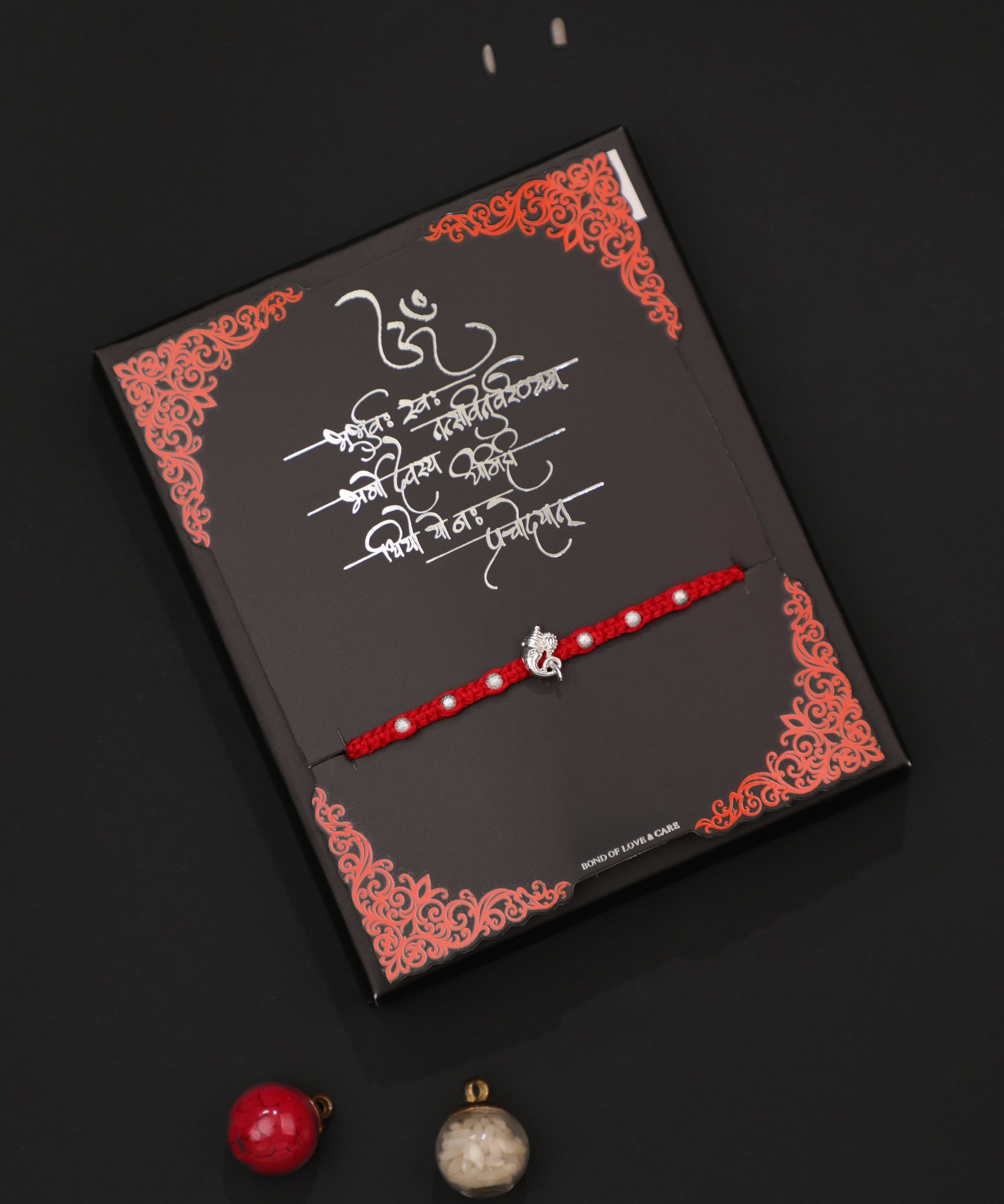 Rhodium finish Rakhi with Ganesha charm and white beads on a red thread