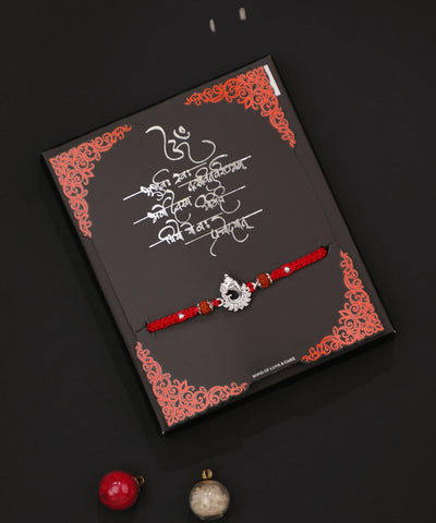 Rhodium finish Rakhi with intricate peacock design and clear stones on a red braided thread