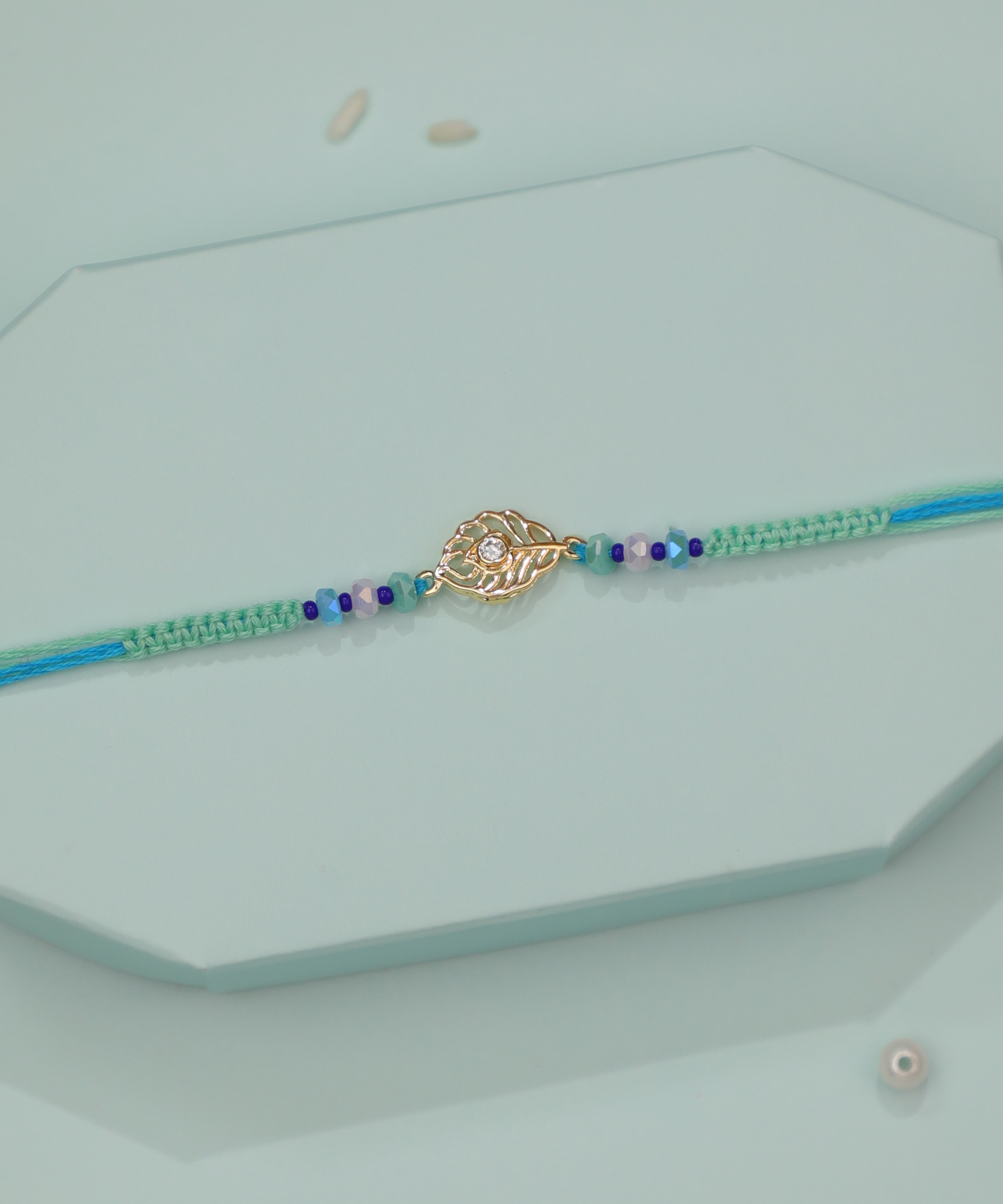 Gold-tone leaf motif Rakhi with clear CZ and blue-green beaded thread