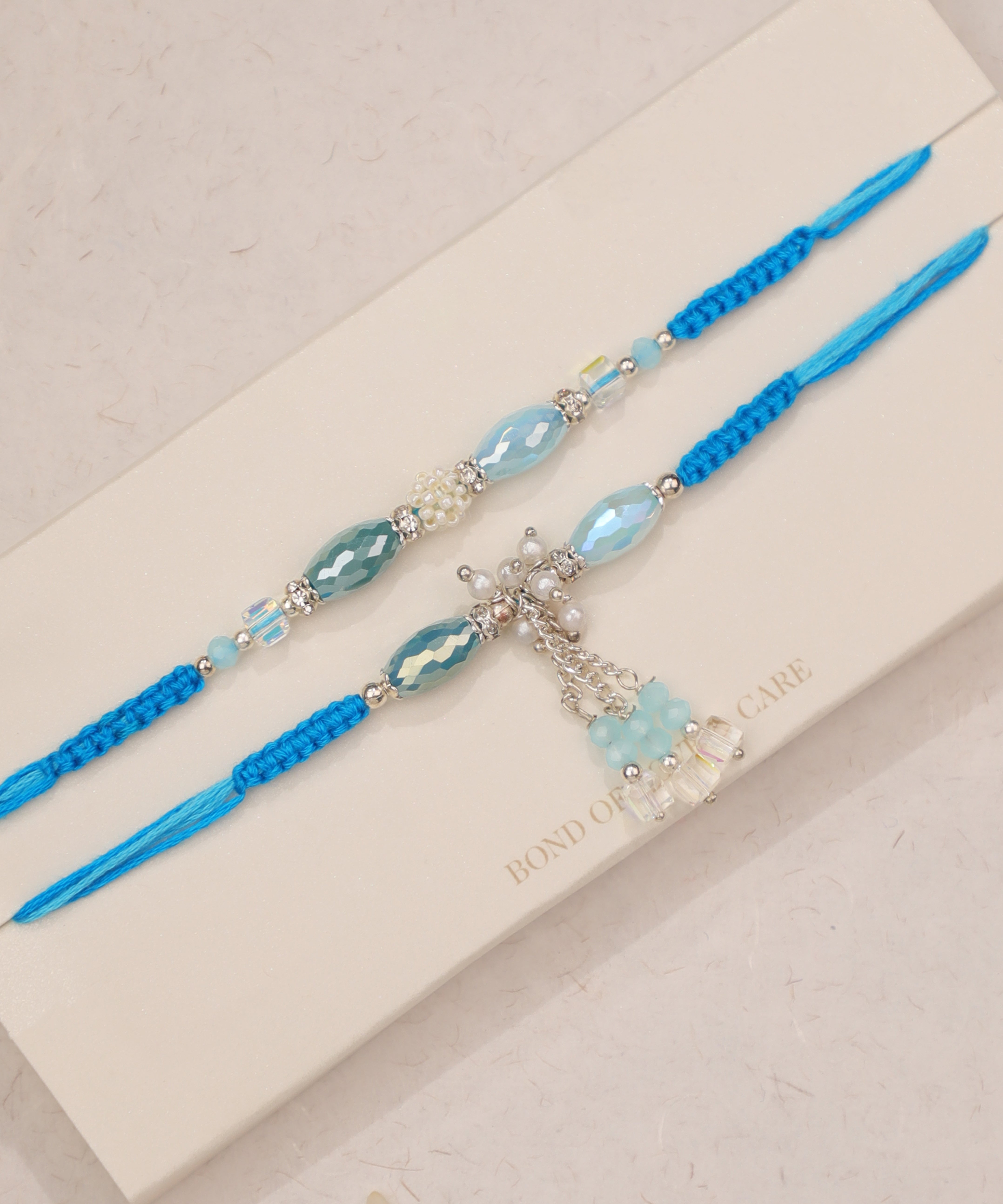 Silver-tone Rakhi set with aqua glass beads, faux pearls, and blue string