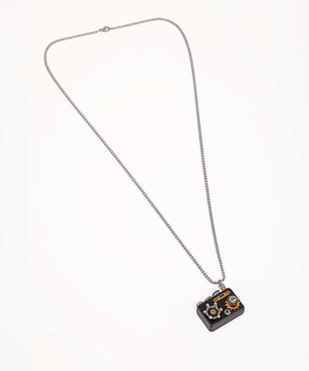 Silver-tone necklace with dark camera pendant featuring mixed metal gears and a small crystal detail