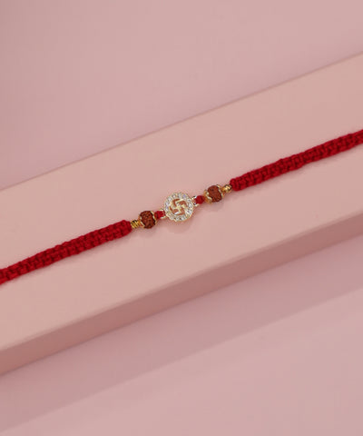 Gold-tone Rakhi with Swastika motif, clear stones, and brown beads on a red braided thread
