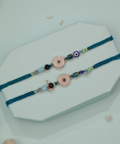 Gold-tone Rakhi set with textured circular charms, evil eye and assorted glass beads on teal woven thread
